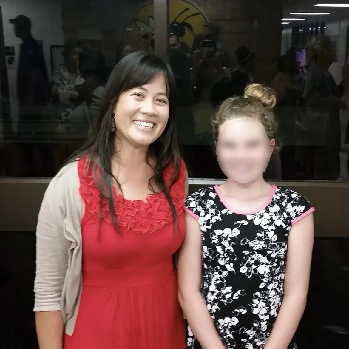 Ms. Lo and her former student at the 5th grade graduation ceremony: Two smiling females, an adult and a young girl, standing together inside a school before the 5th grade ceremony began.