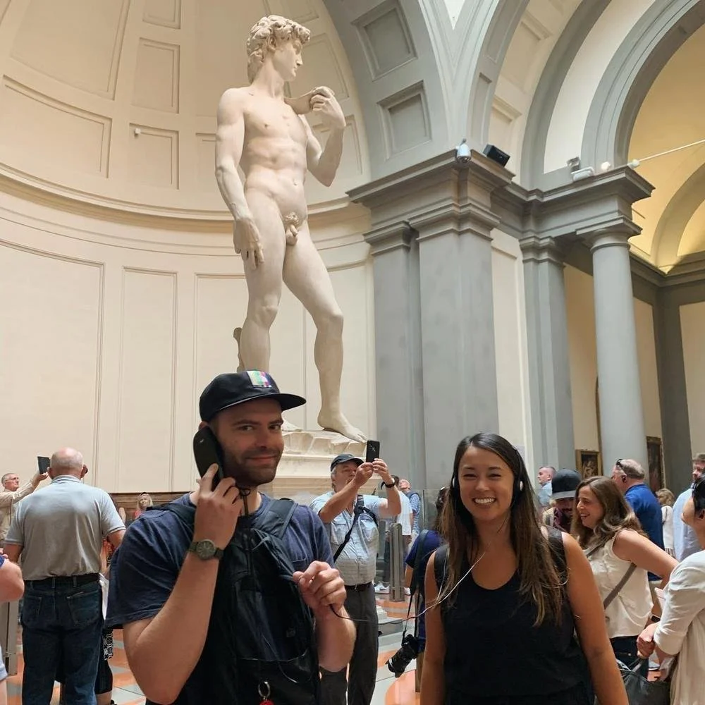 People in an art museum admiring the statue of David by Michelangelo in the background.