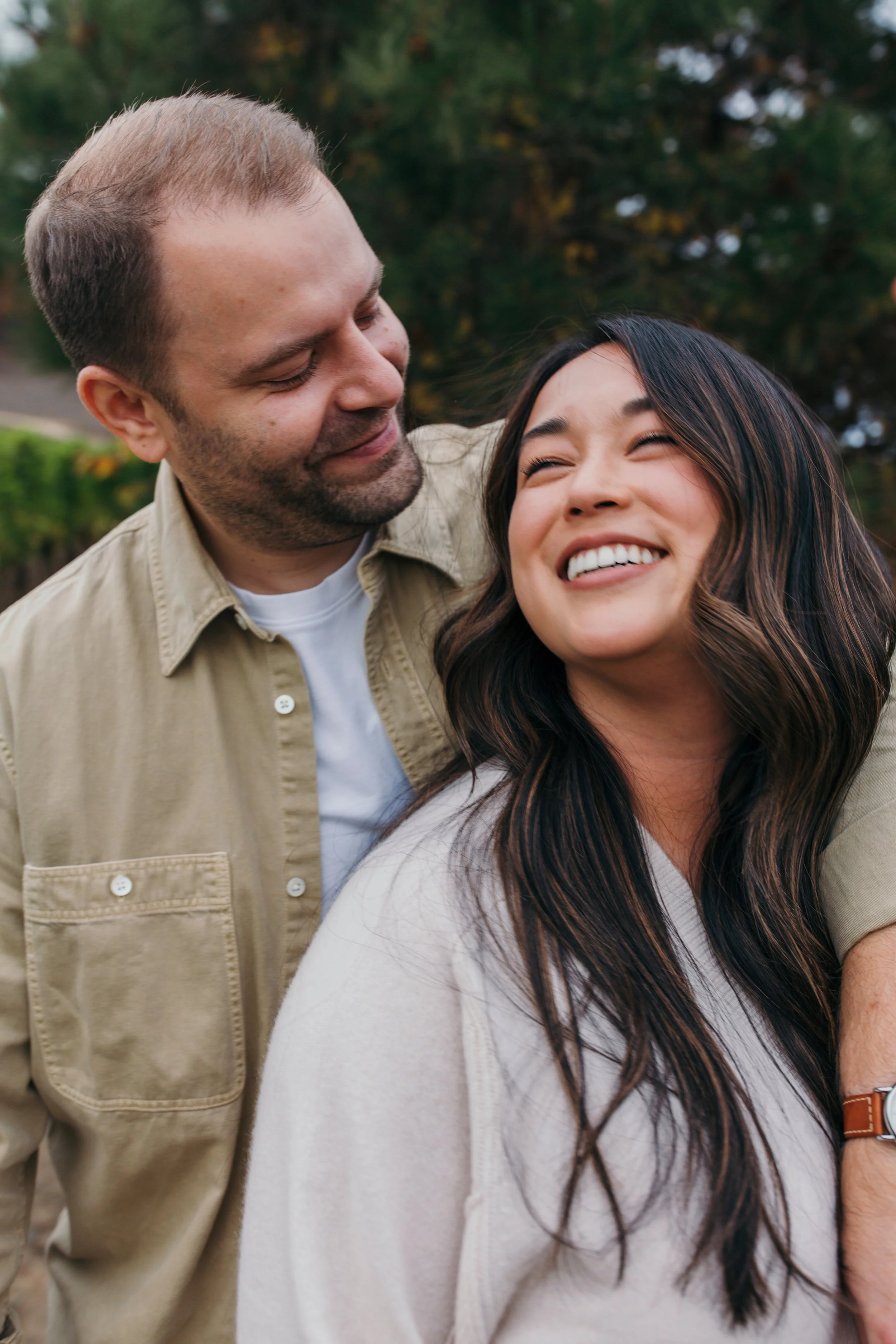 A happy couple smiling and embracing outdoors with trees in the background.