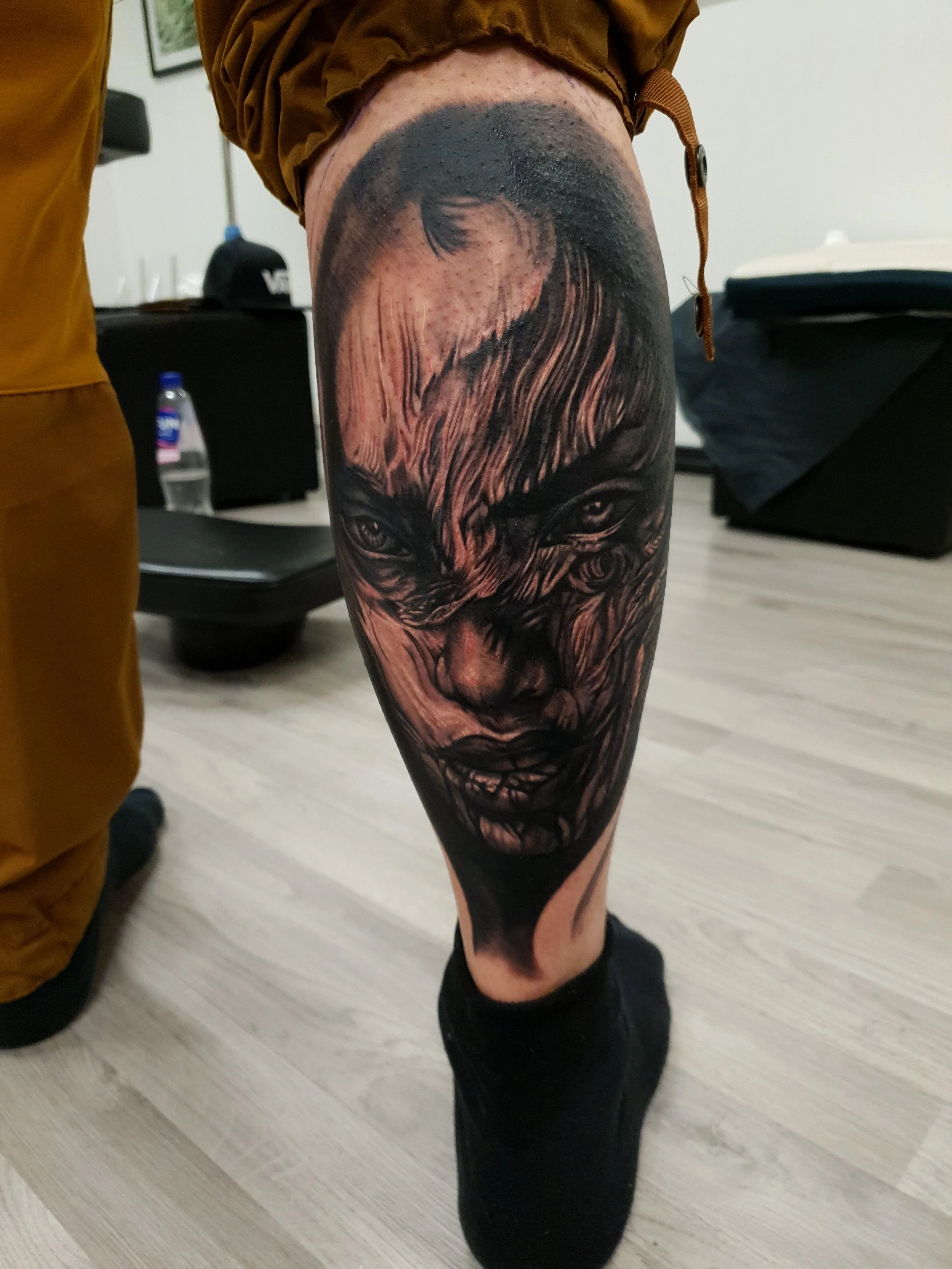 Tattoo of a woman's face with intense expression, dark shading, and detailed features on a person's thigh.