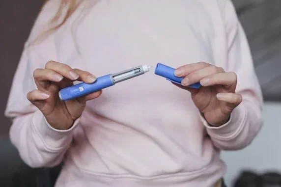 Person holding an opened blue inhaler with the cap removed.