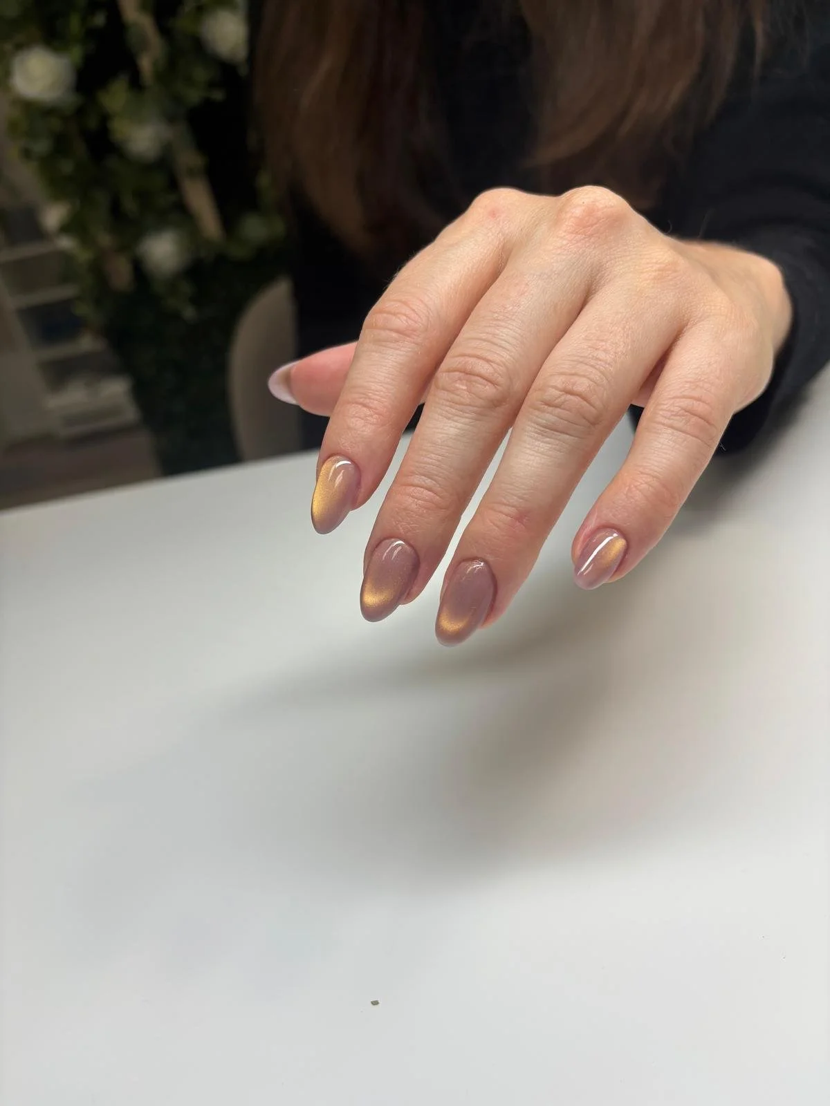 A person's hand resting on a white surface with nails painted in a gradient metallic gold and natural color.