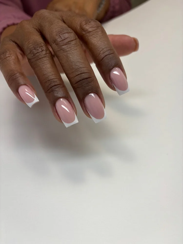 A hand with dark skin tone resting on a white surface, showcasing nails with pink polish and white French tips.