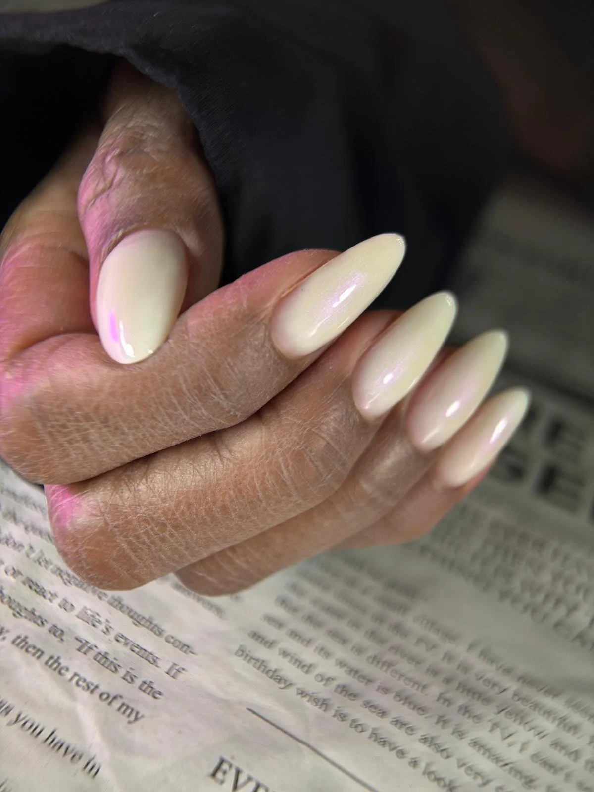 Close-up of a hand with long, cream-colored, almond-shaped nails, holding a piece of paper.