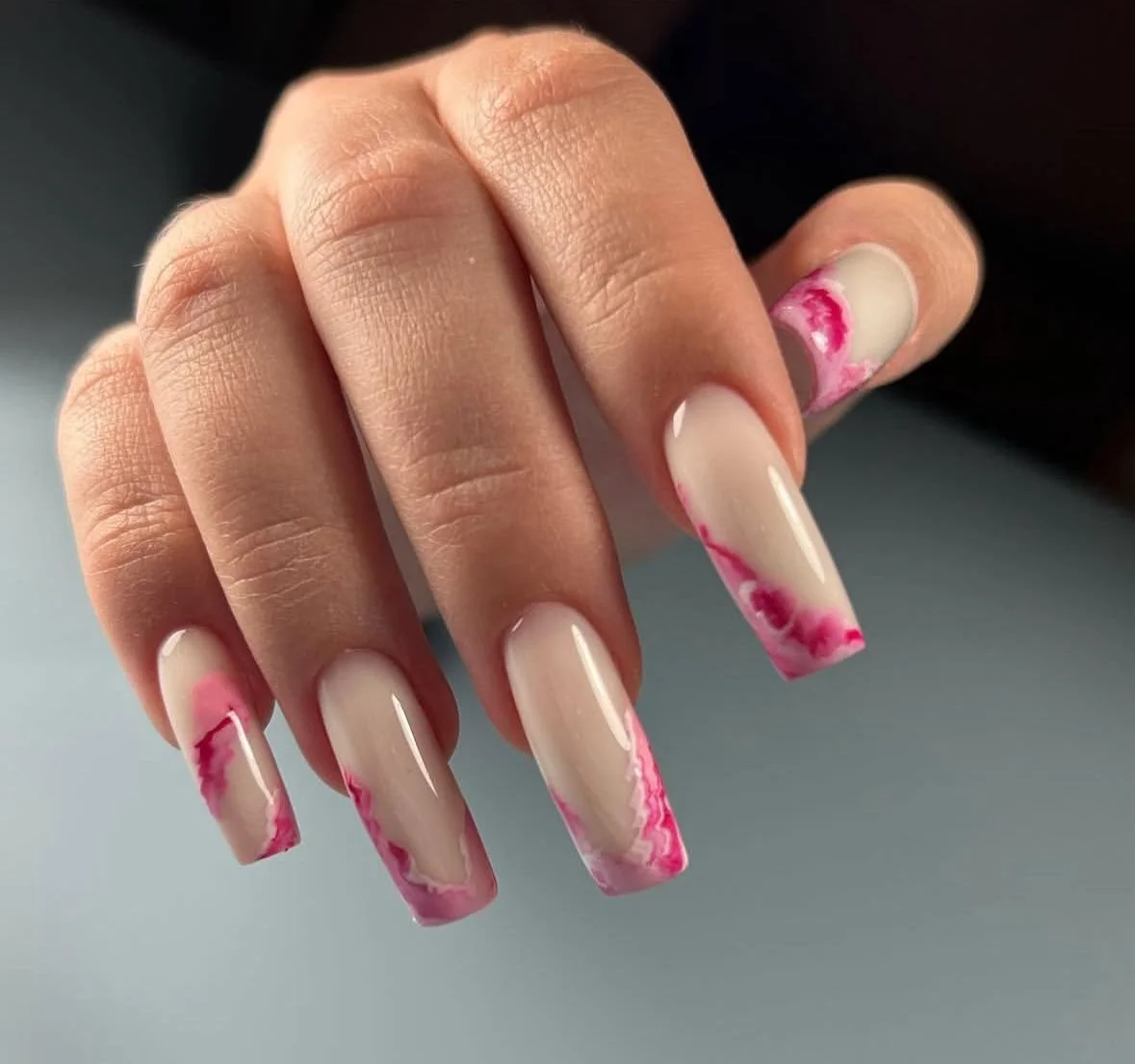 Hand showing nails with a nude base and pink marble tips.