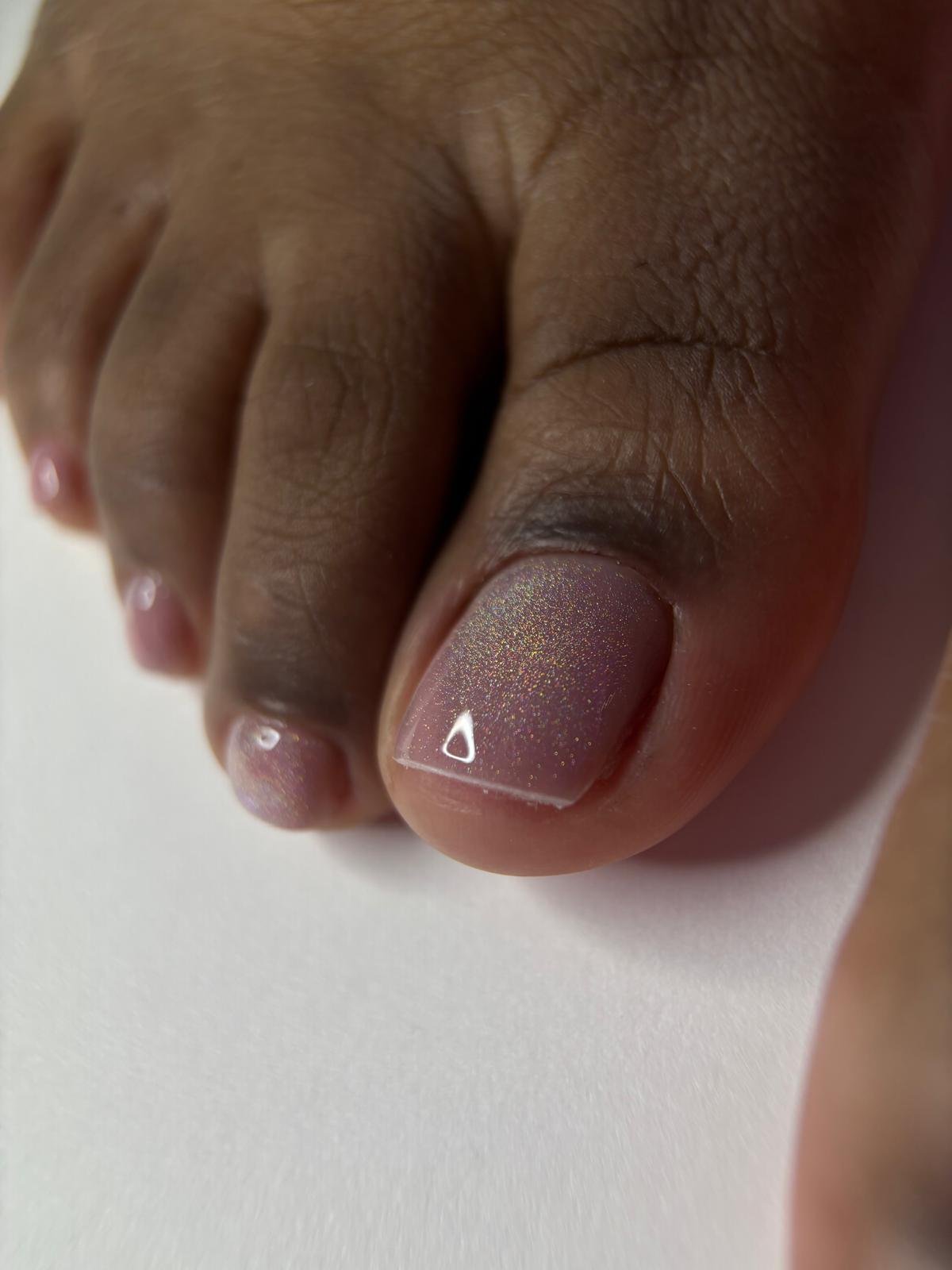 Close-up of a person's toenail painted with glittery, nude-colored nail polish.