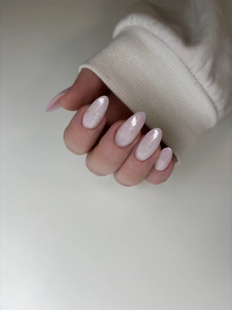 Hand with manicured nails painted in a pearly white color, partially covered by a cream-colored sweatshirt sleeve.