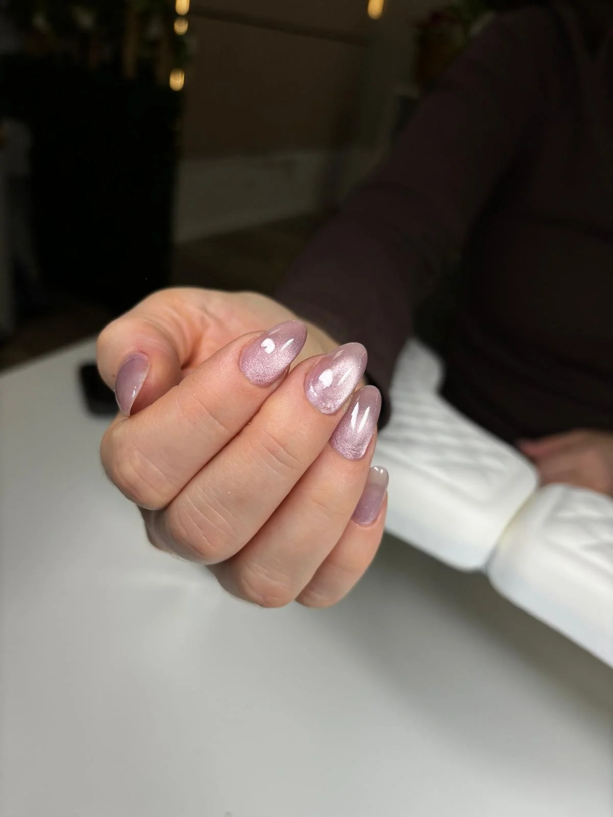Close-up of a woman's hand with manicured nails that have a shiny, translucent pink polish, against a blurred background.