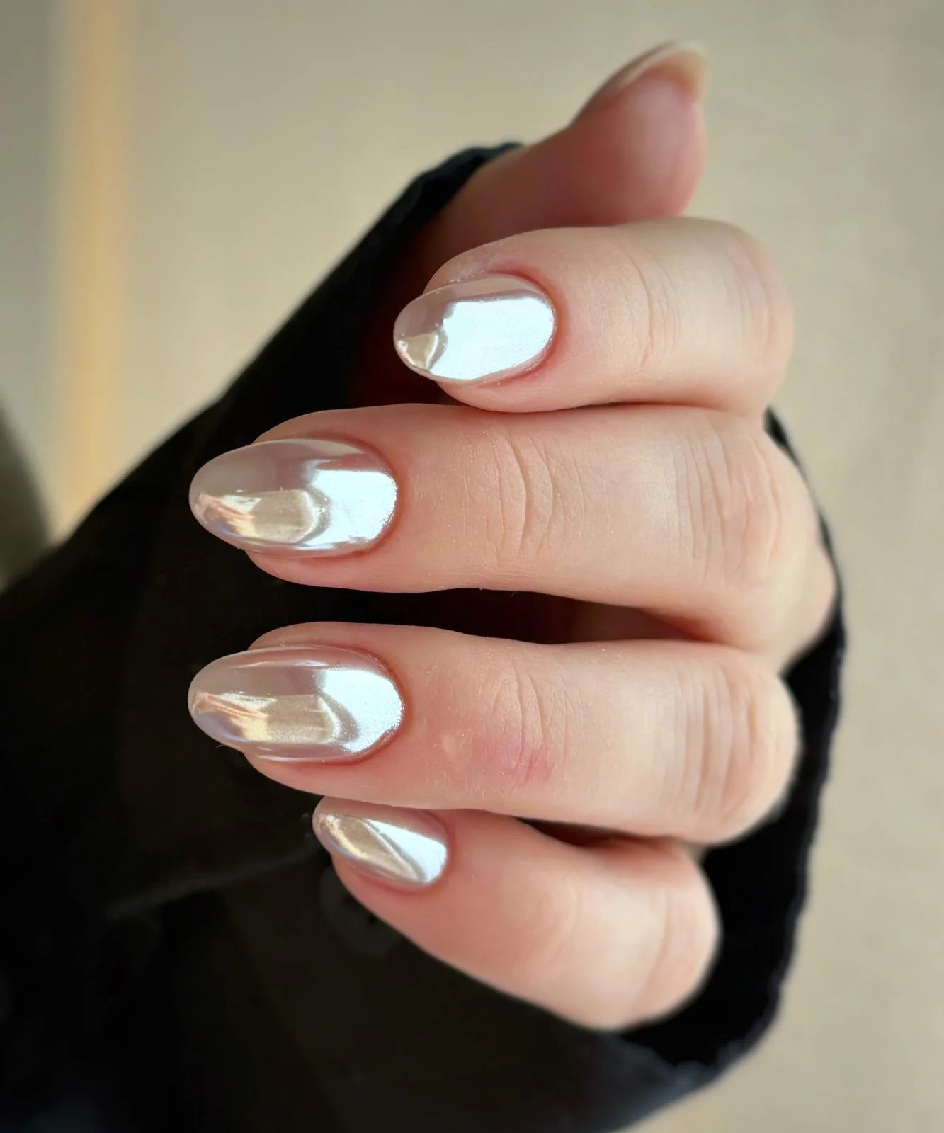 Close-up of a hand with shiny, metallic silver nail polish on fingernails, partially covered by a black garment.