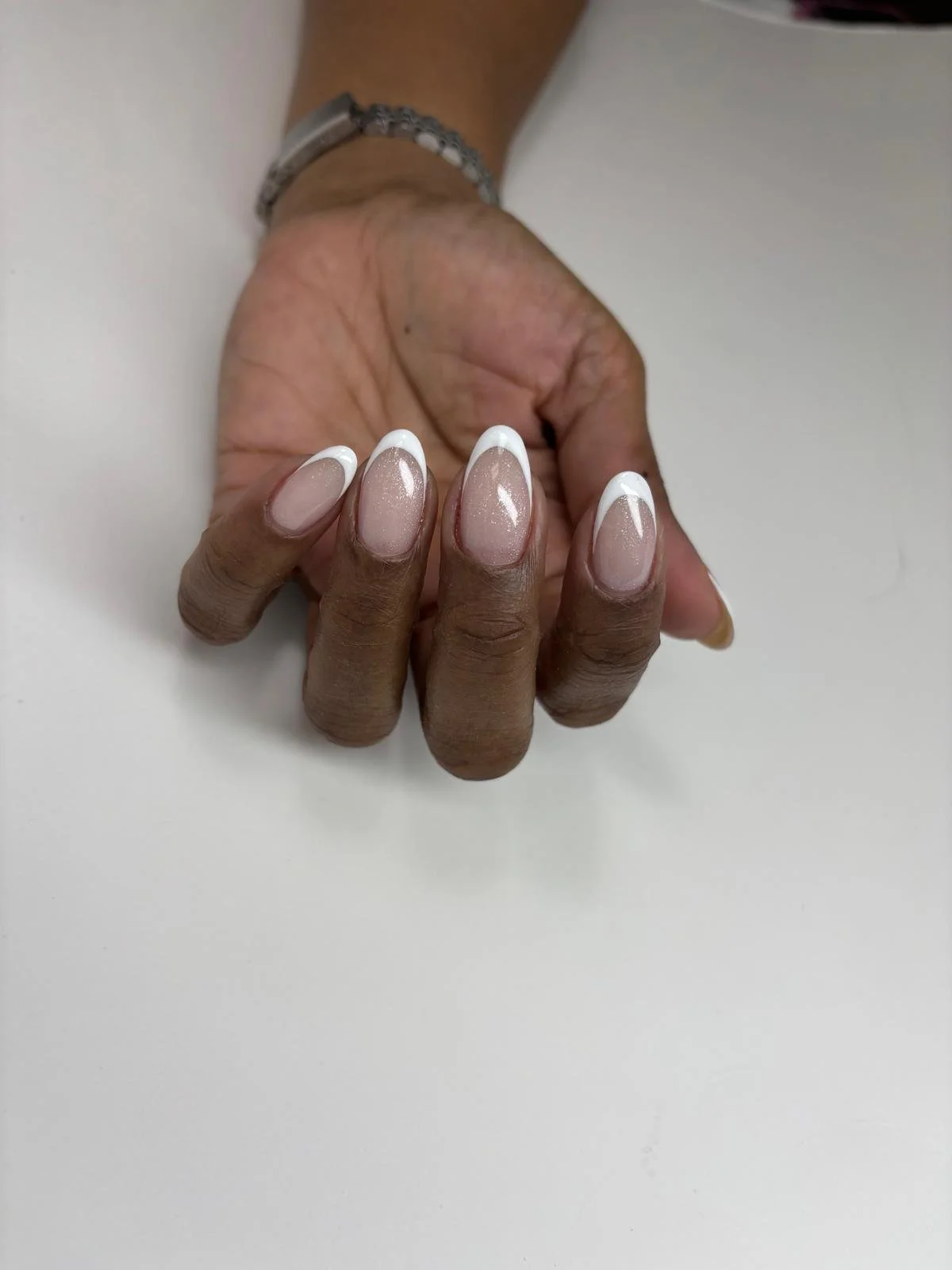 Close-up of a hand with manicured nails exhibiting a French tip design with white tips and a nude base, resting on a white surface.