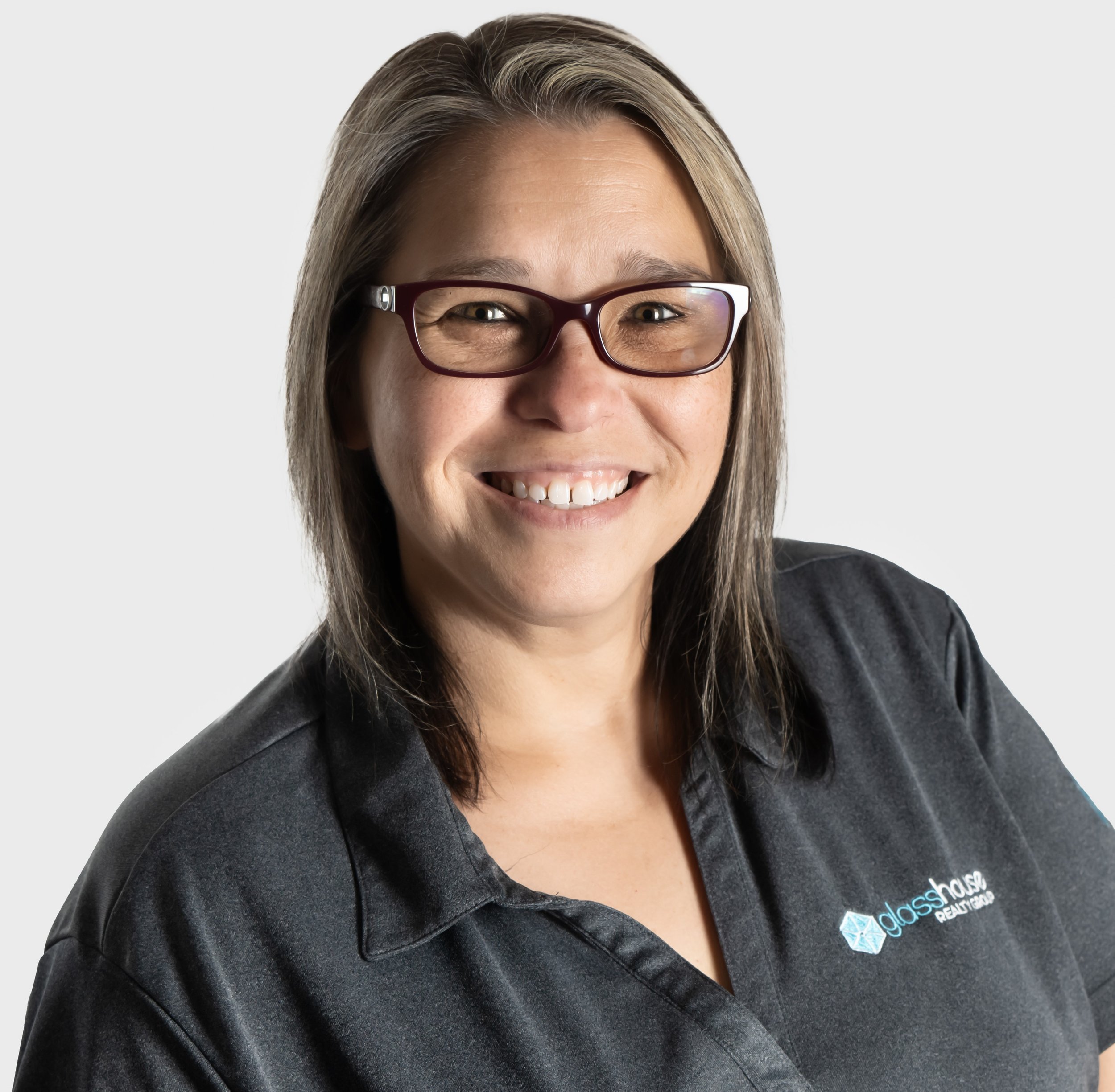 A woman with brown hair and glasses smiling, wearing a black shirt with a logo that says 'glosshouse'.