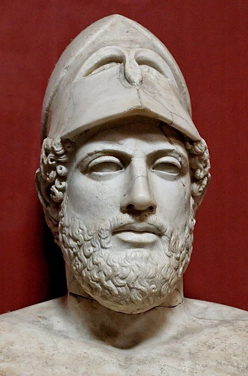 Ancient Greek marble bust of a bearded man wearing a helmet with a crest, set against a red background.