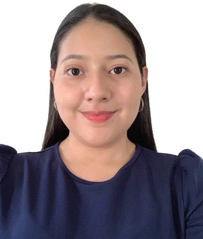 A young woman with long dark hair, wearing a navy blue top with puffed sleeves, smiling, and looking directly at the camera against a white background.