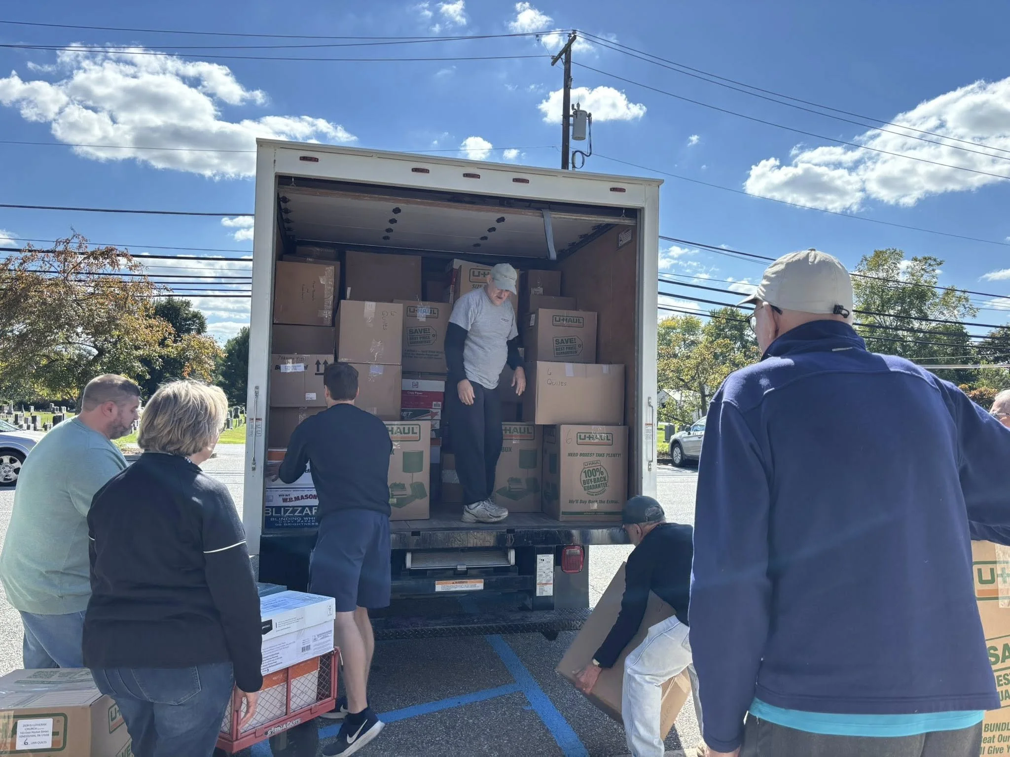 People packing boxes from a U-Haul truck on a sunny day in a parking lot.