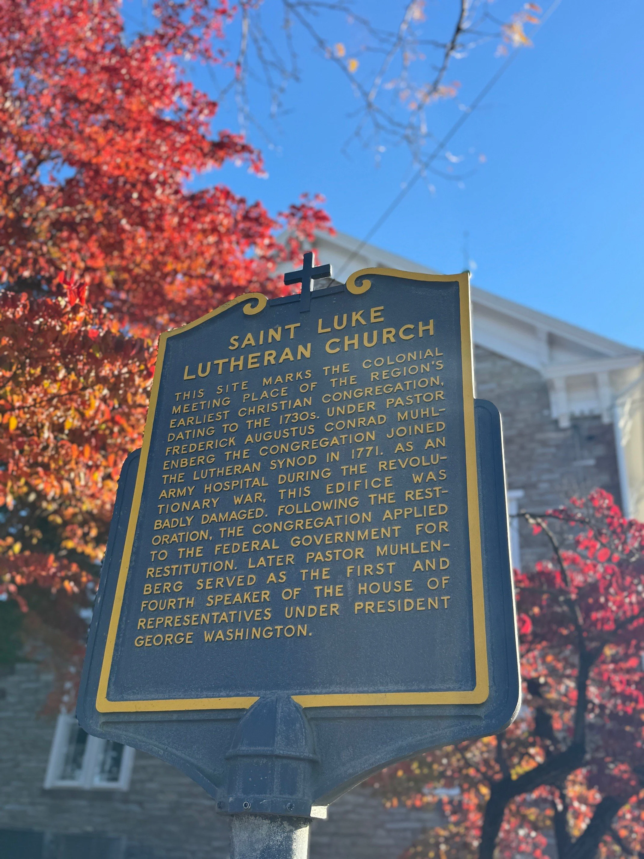 Historical plaque in front of Saint Luke Lutheran Church with fall foliage and blue sky in the background.