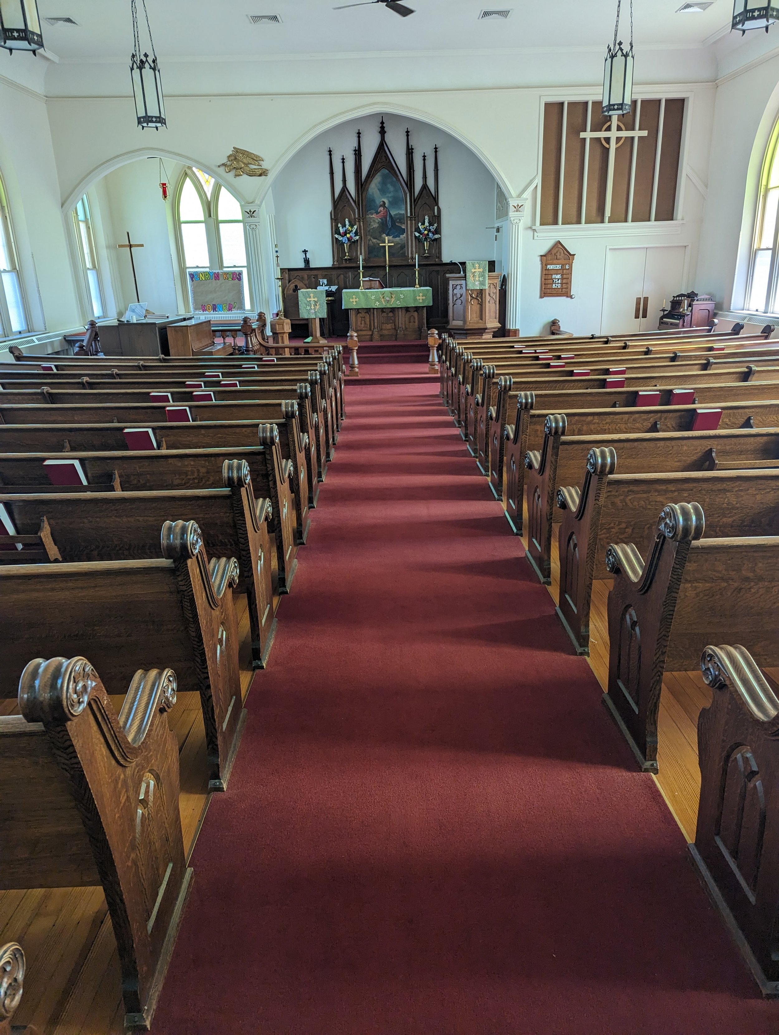 Interior view of a church with wooden pews, an altar at the front, and stained glass windows.