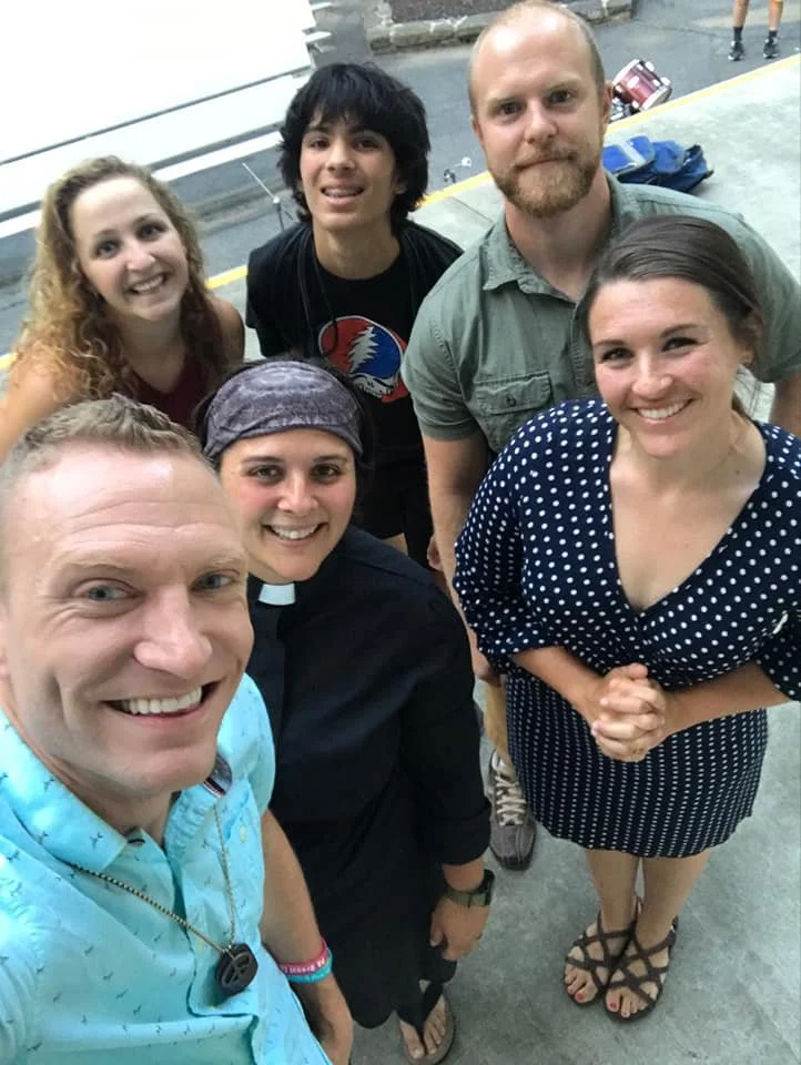 Group of six people, including a pastor, posing for a selfie outdoors.