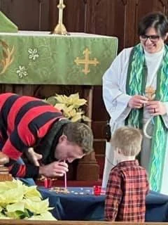 A man appears to be playing a game with a young child, while a woman in religious attire looks on and smiles indoors decorated for a religious celebration.