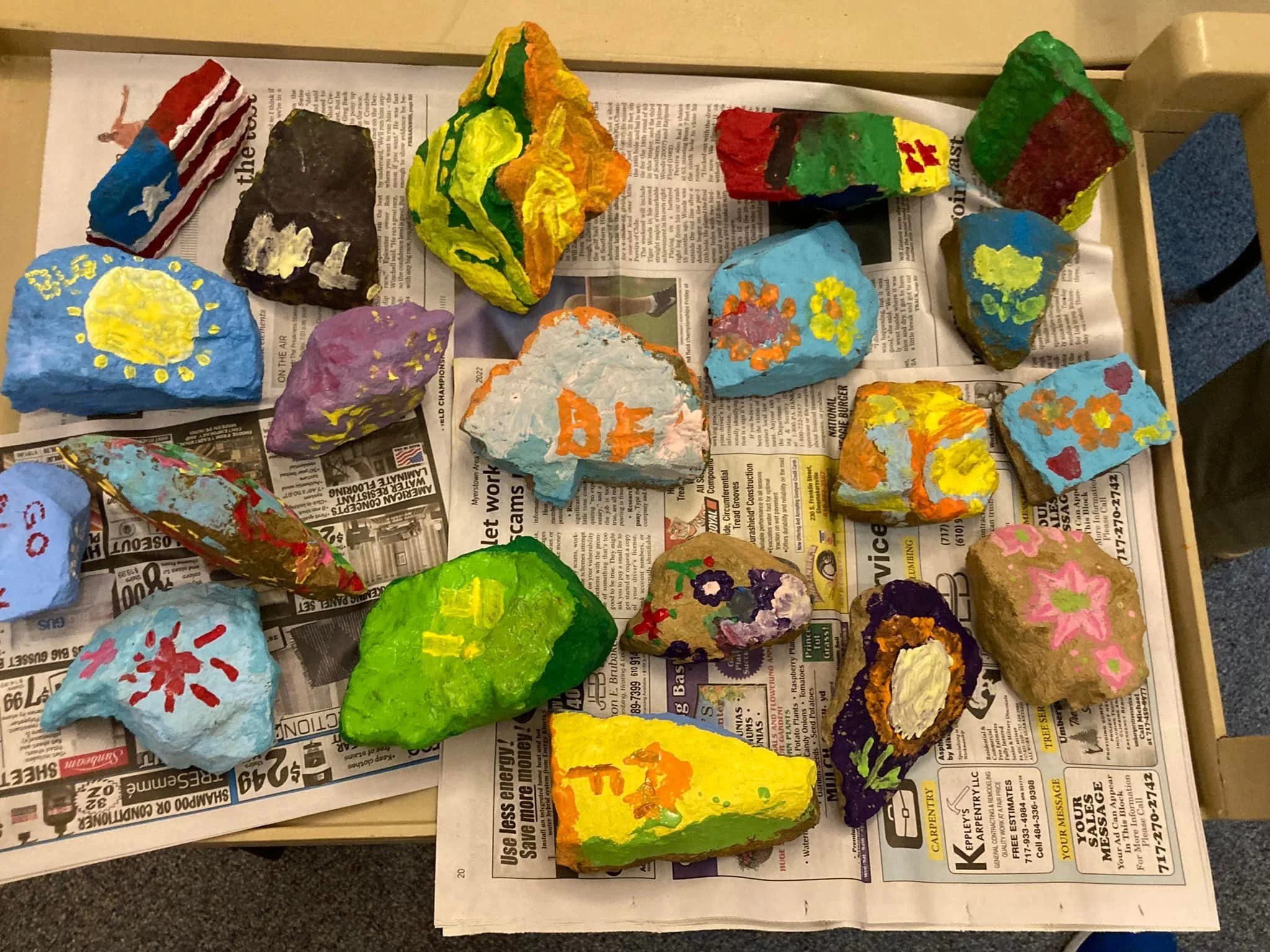 Colorfully painted rocks arranged on a newspaper-covered table.