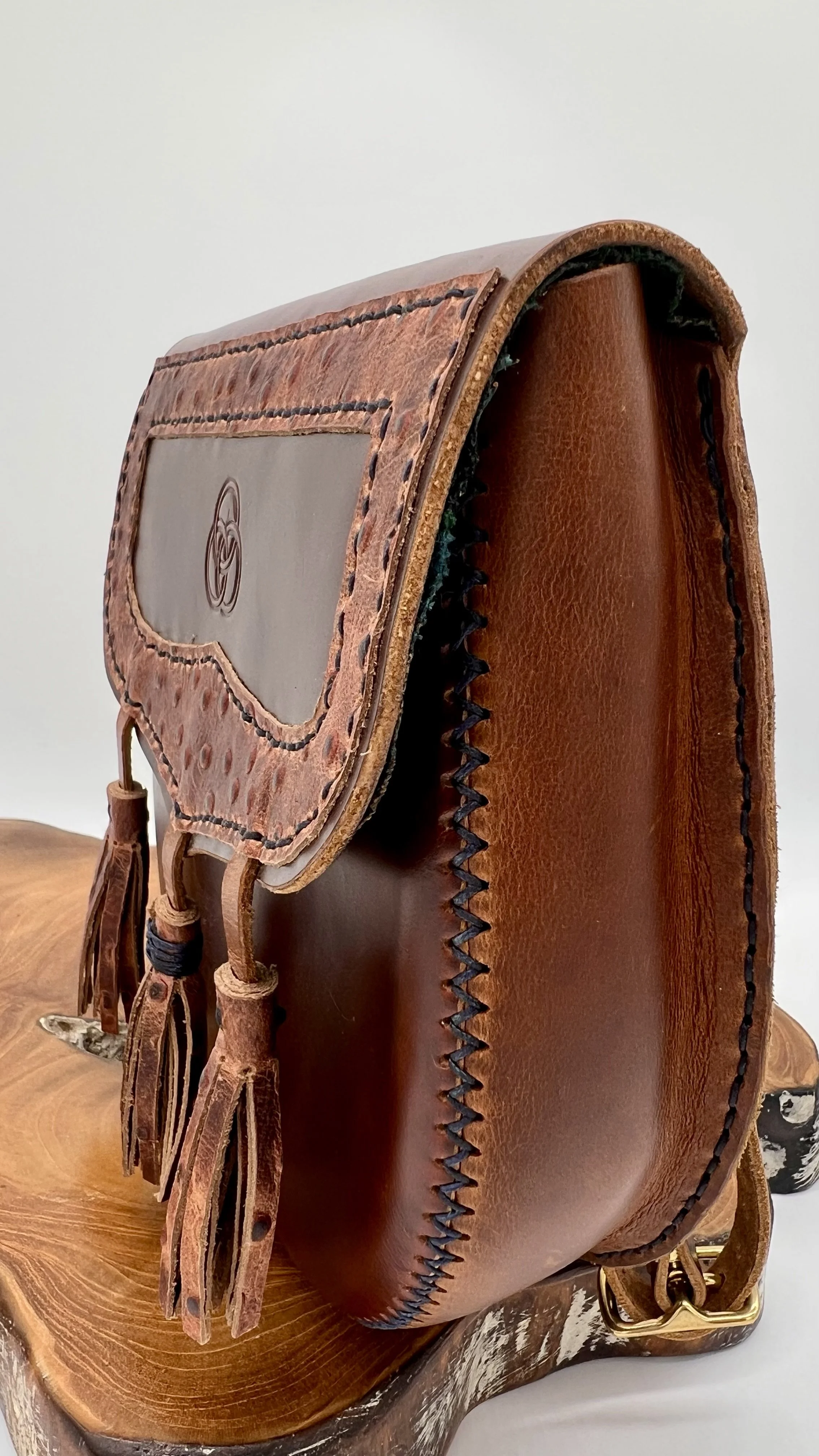 A brown leather saddle with decorative stitching and tassels, resting on a wooden surface.