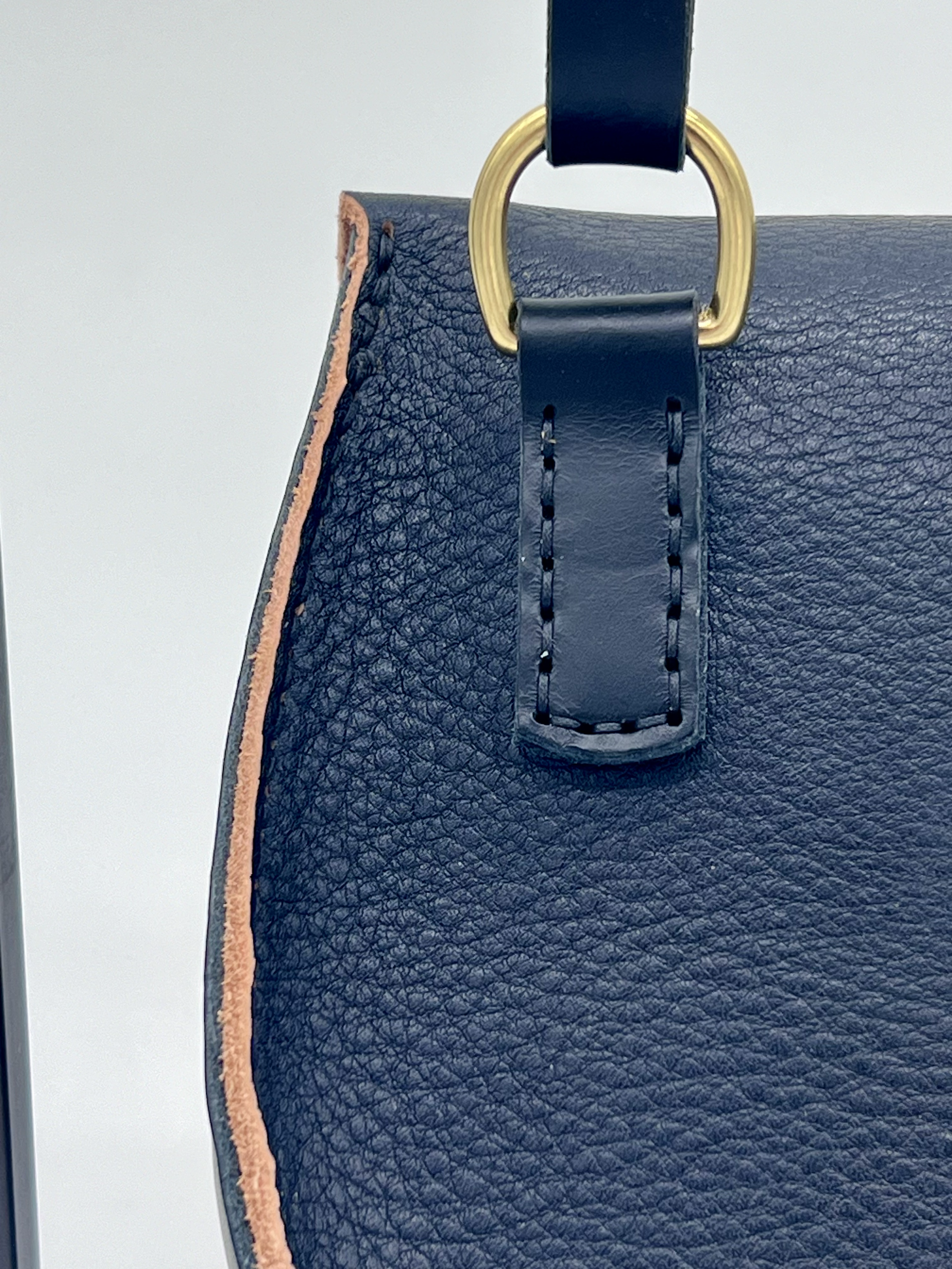 Close-up of a navy blue textured leather handbag with a gold ring handle and pink piping on the side.