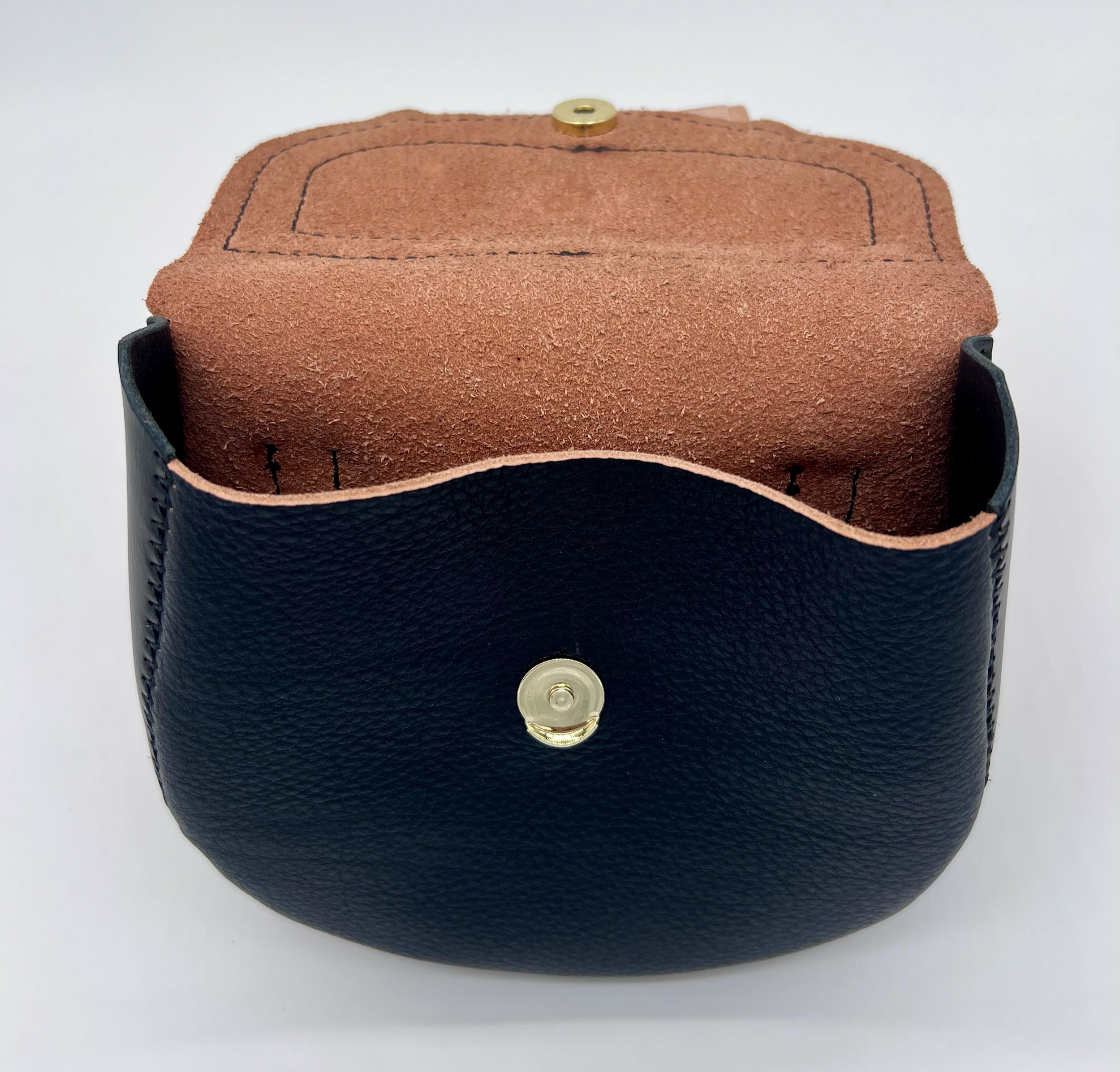 Close-up of a black leather camera case with a textured surface and gold snap buttons, revealing a brown leather interior.