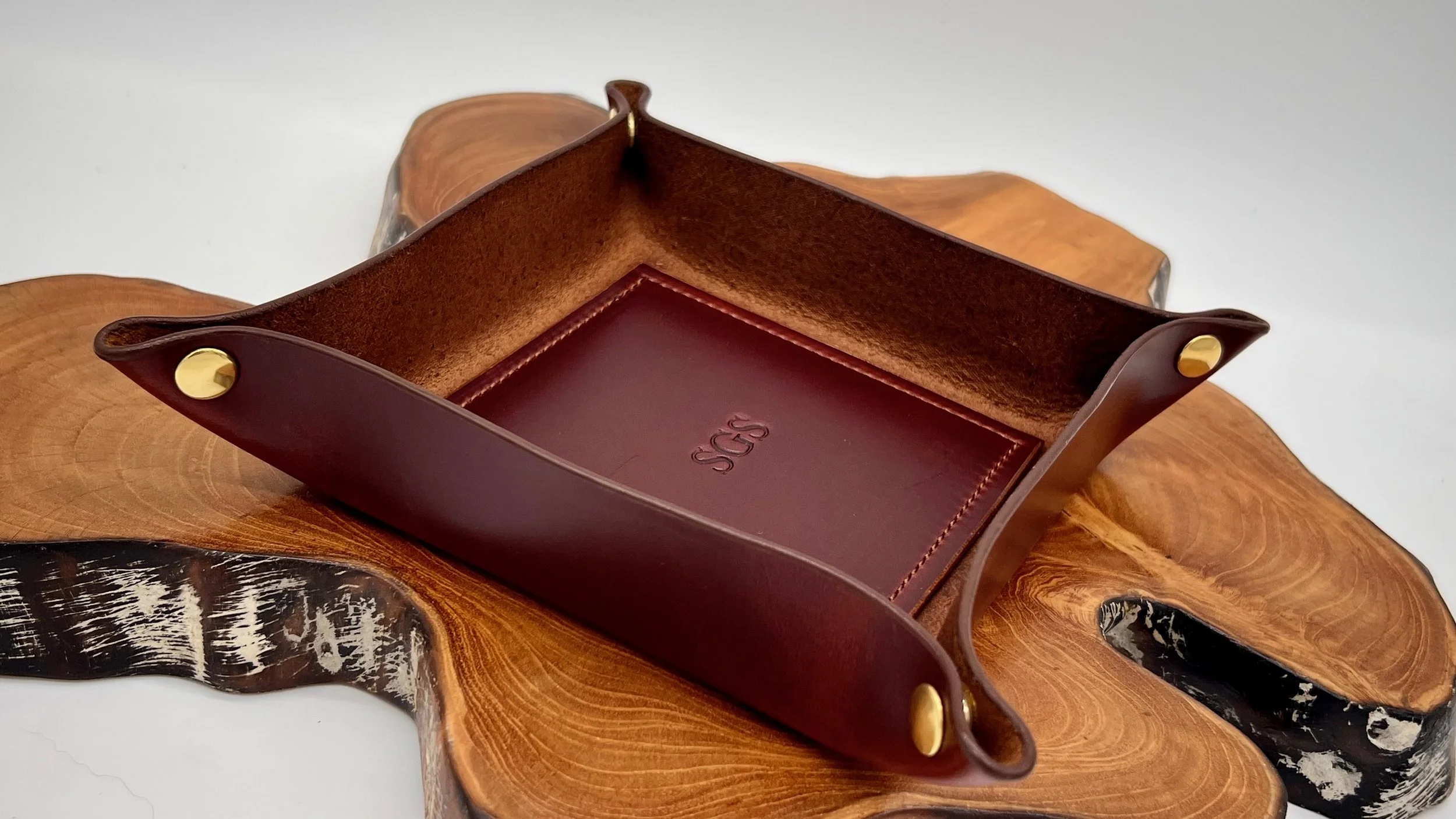 Open leather tray with gold rivets, placed on a wooden surface