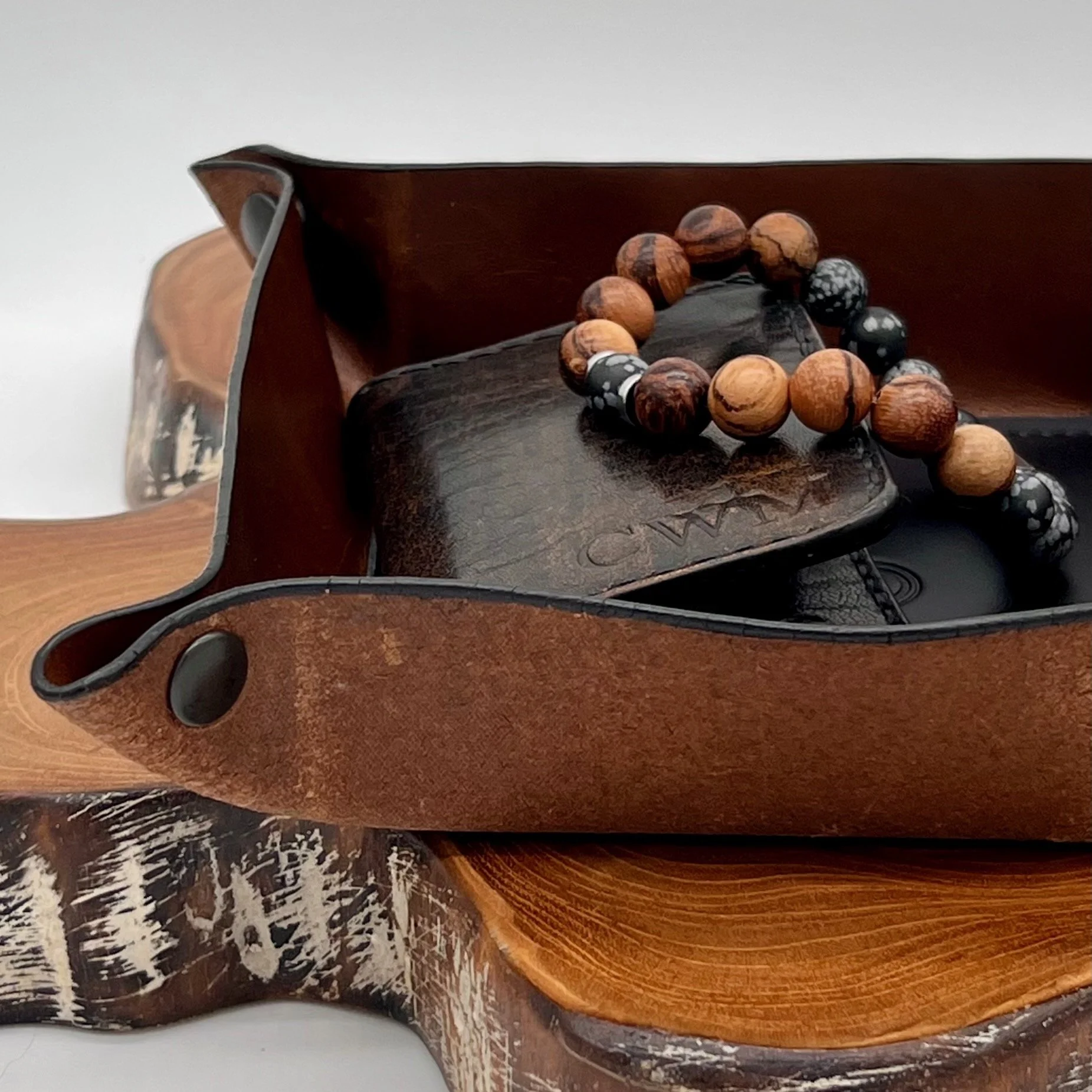 Brown leather wallet, wooden bead bracelet, black phone, and wooden tray on a wooden surface.