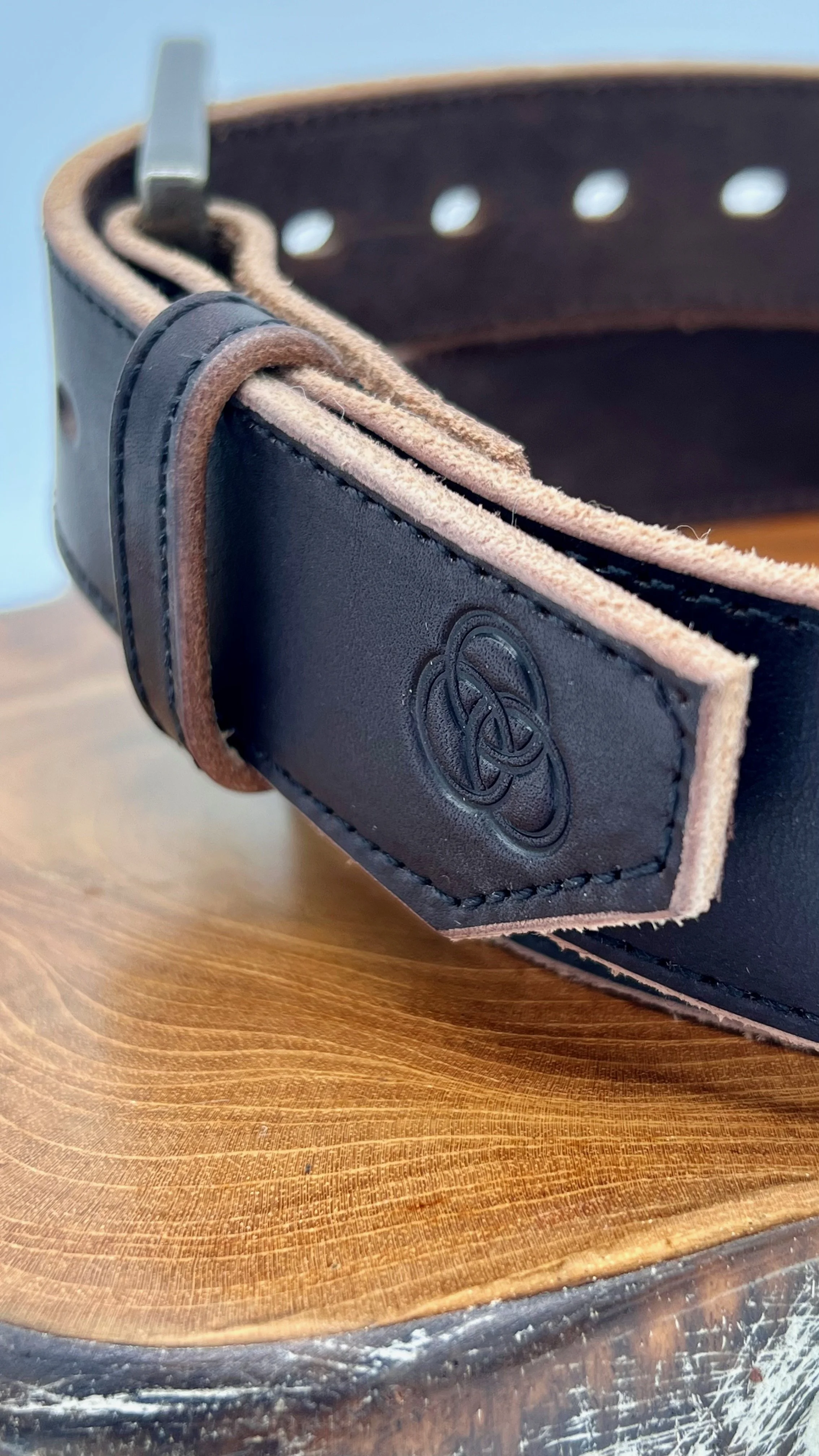 Close-up of a black leather belt with a Celtic knot design, resting on a wooden surface.