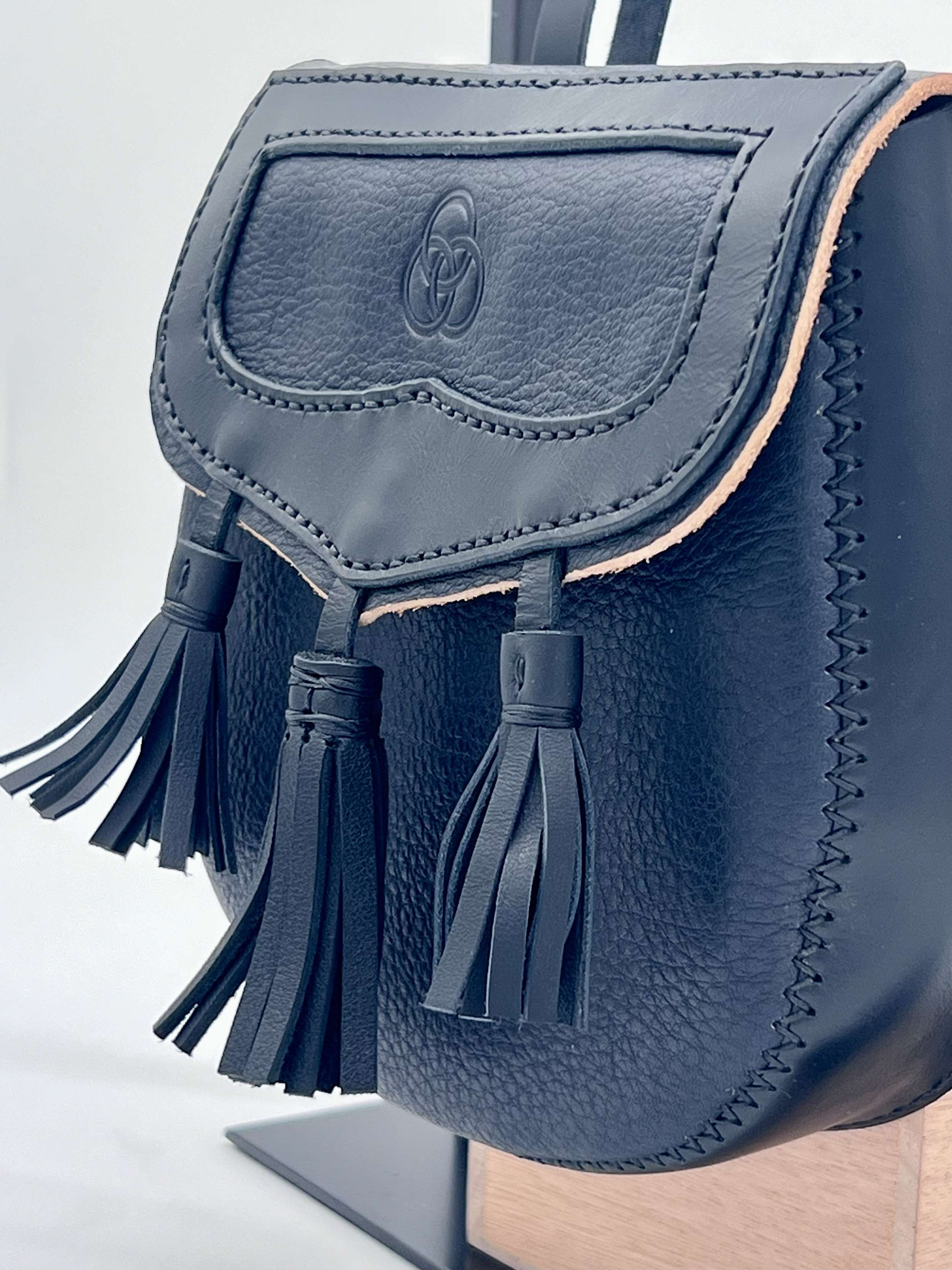 Black leather handbag with tassel accents and stitching details displayed on a stand.