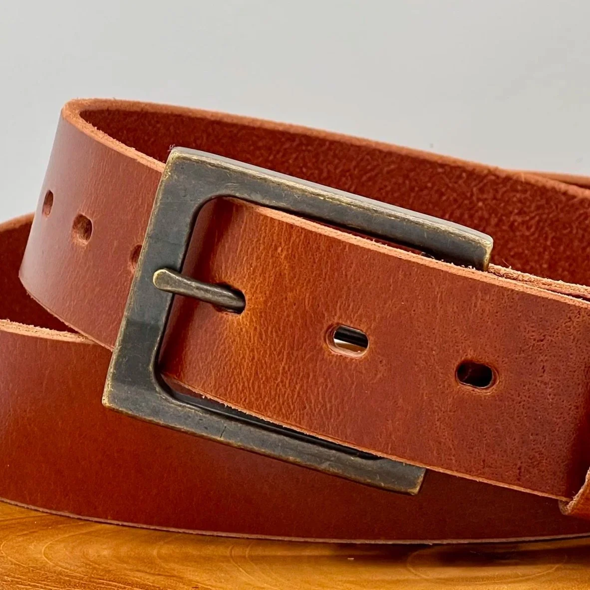 A close-up image of a brown leather belt with a silver metal buckle resting on a wooden surface.