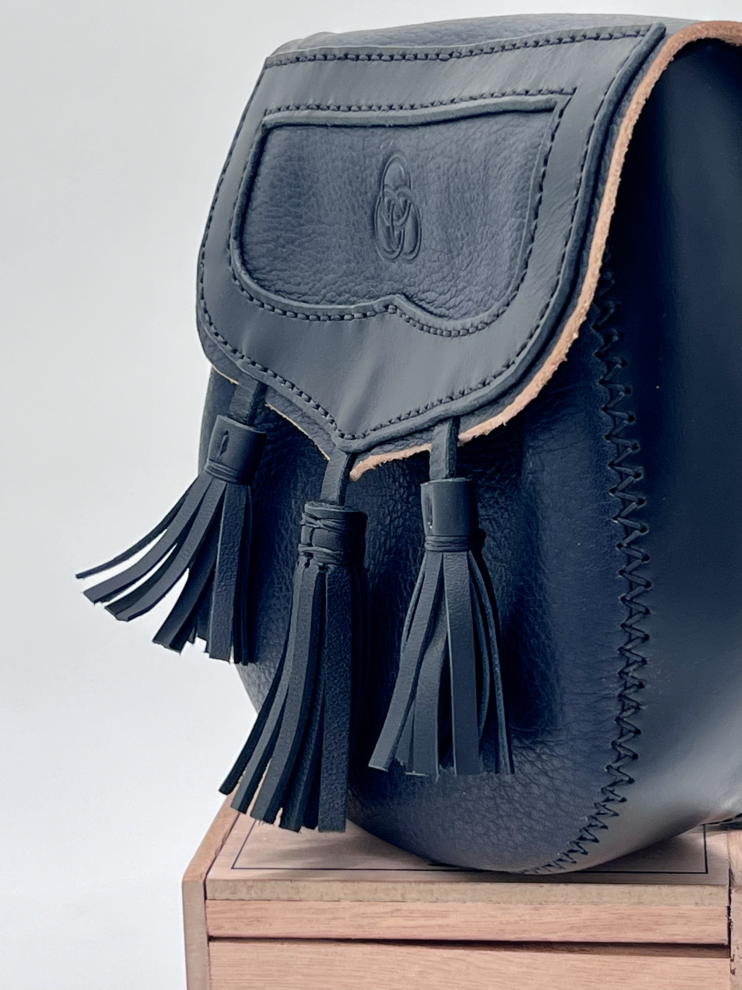 A close-up of a black leather bag with tassel accents, placed on a wooden surface.
