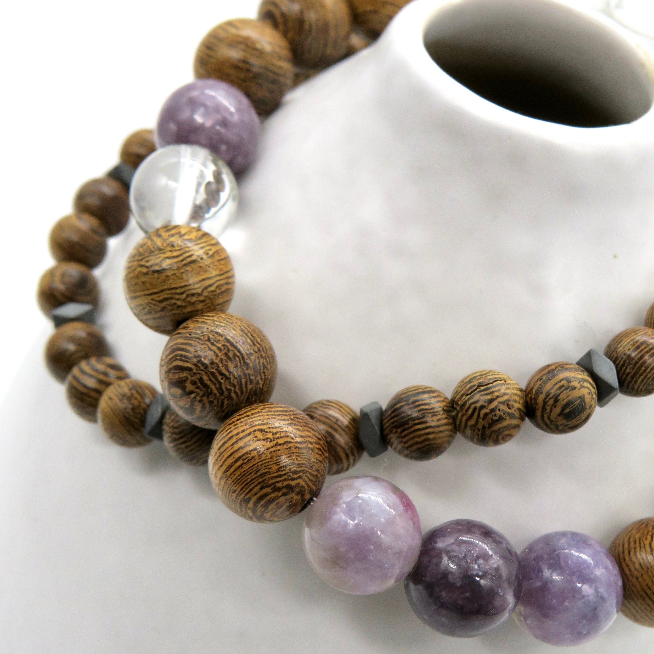 Necklace made with wooden, purple, clear, and black beads displayed on a white ceramic object.
