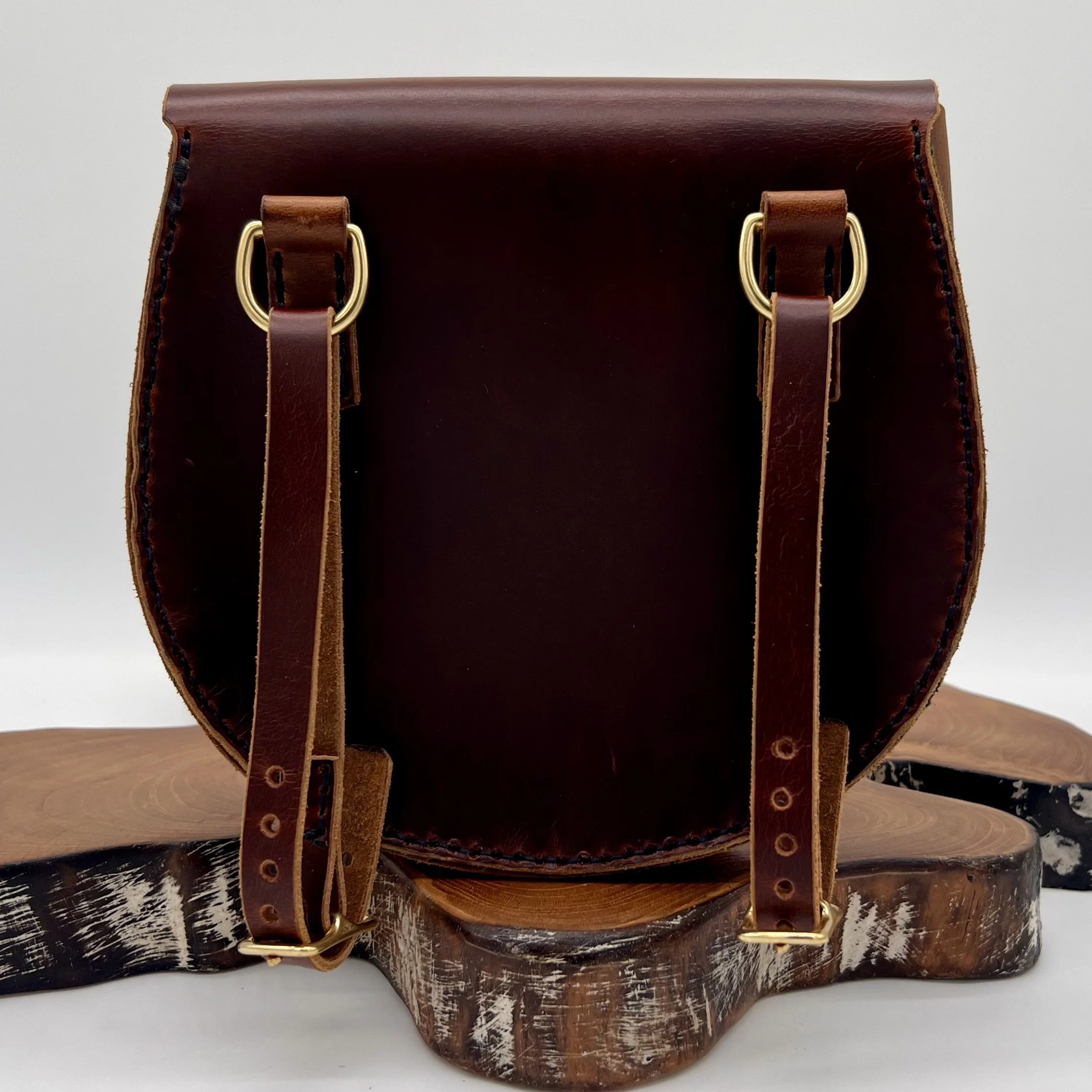 Front view of a brown leather handbag with gold hardware, placed on a wooden surface with a white background.