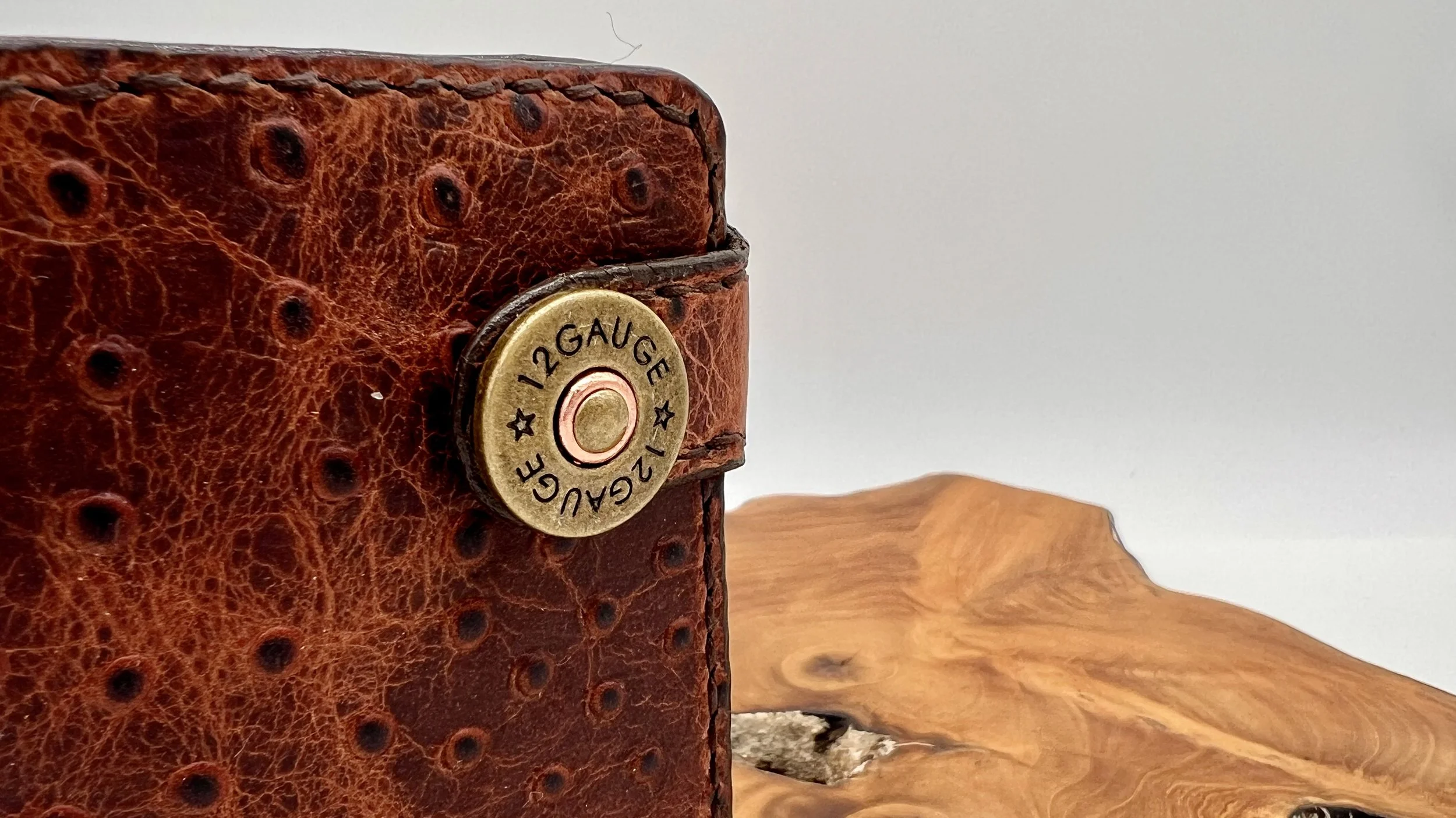 Close-up of a vintage leather-bound box with a brass 12-gauge shotgun shell casing attached as decoration, placed on a wooden surface.