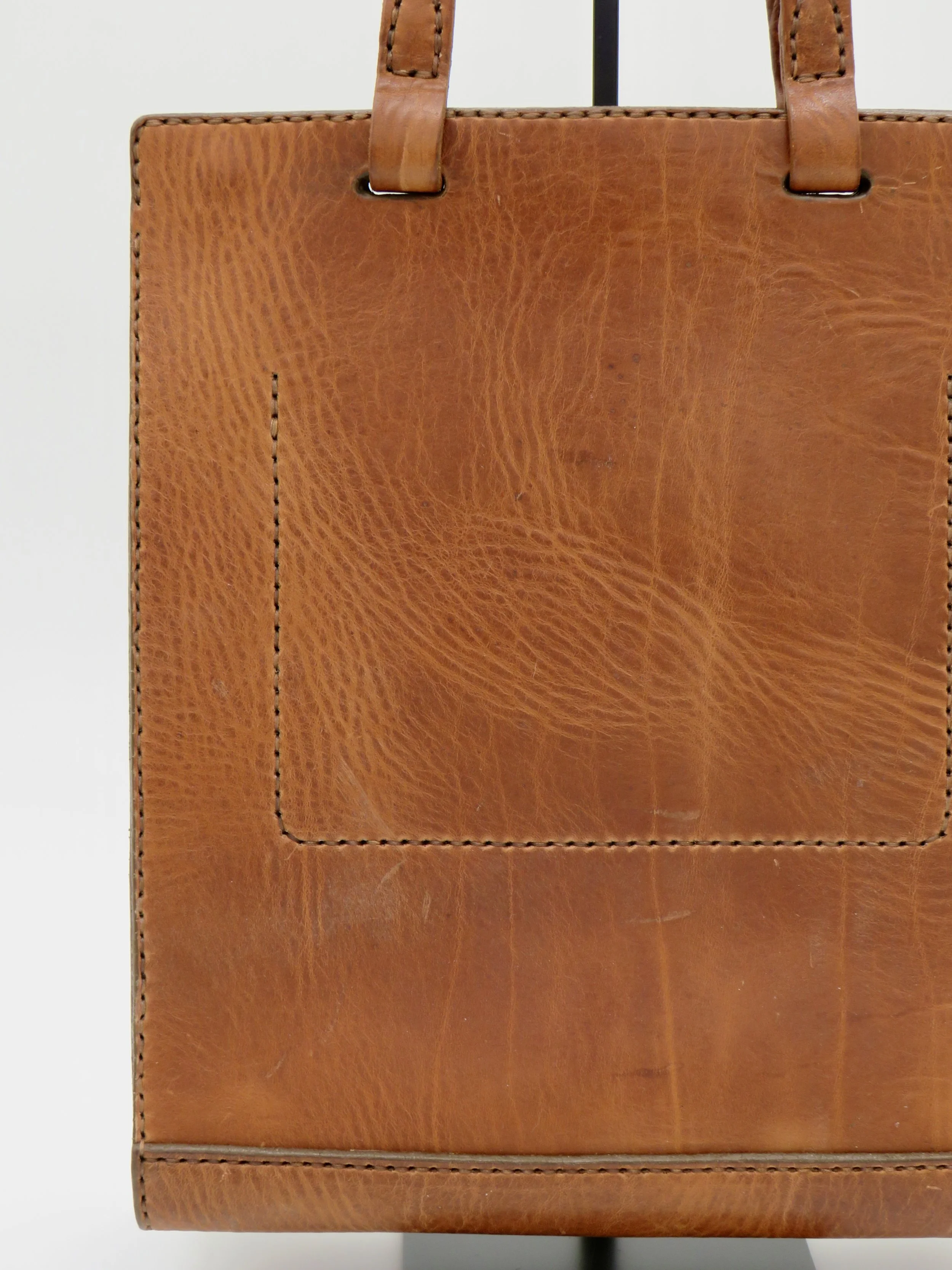 Close-up of a brown leather handbag showing the front pocket and top handles.