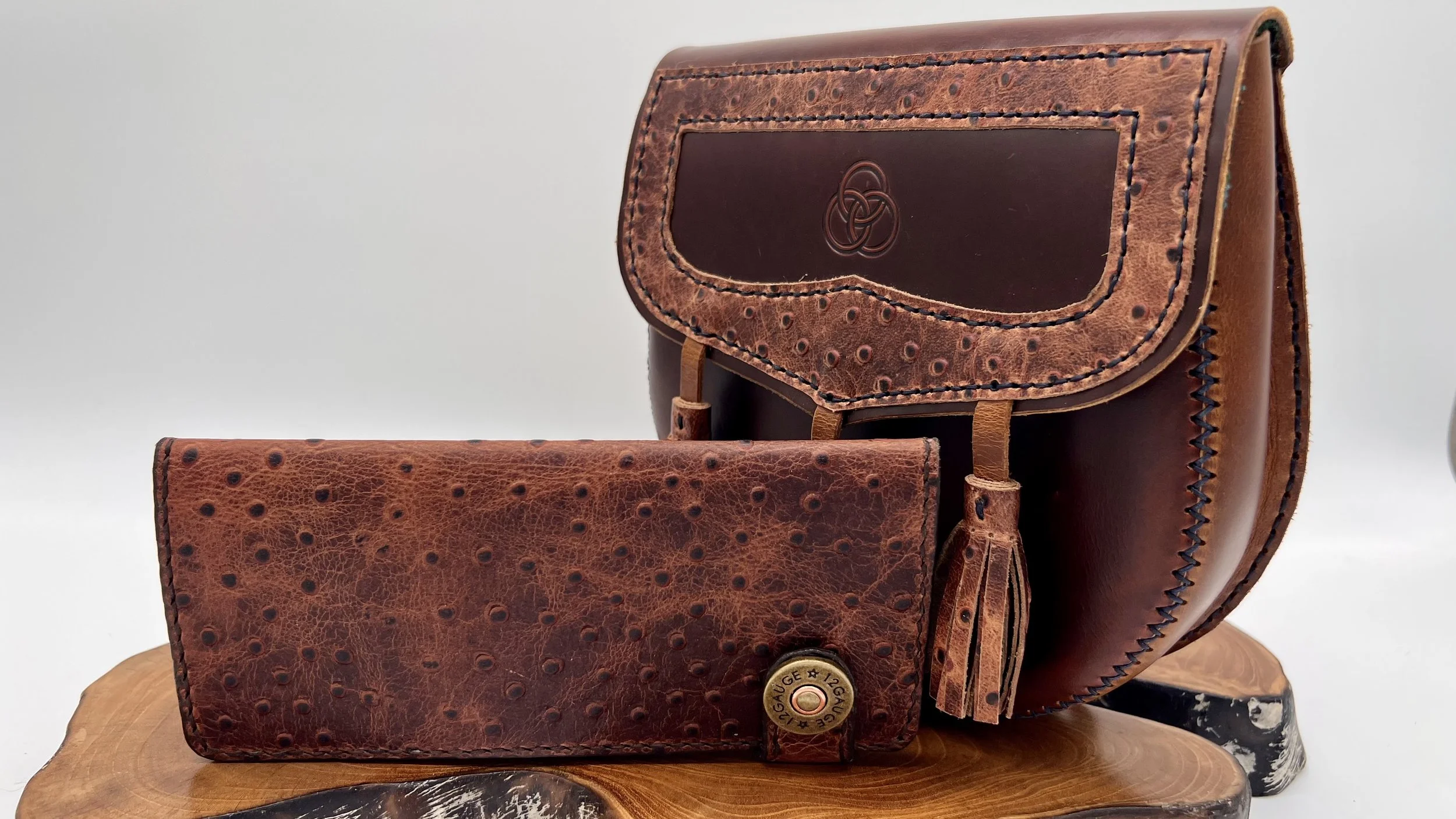 Brown leather handbag with a flap and decorative stitching, placed on a wooden surface, with a matching wallet in front.