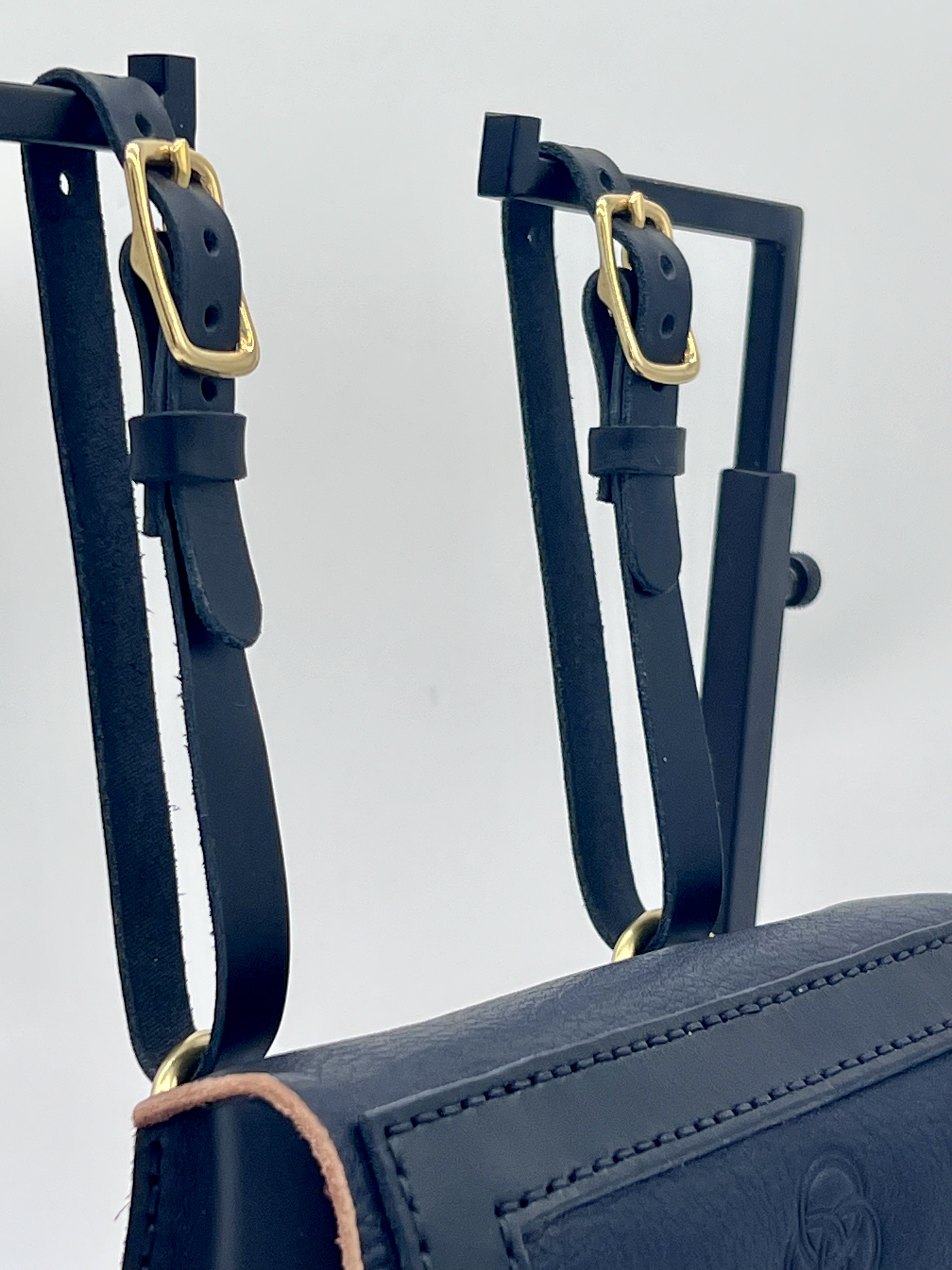Close-up of a black handbag with adjustable straps and gold buckles.