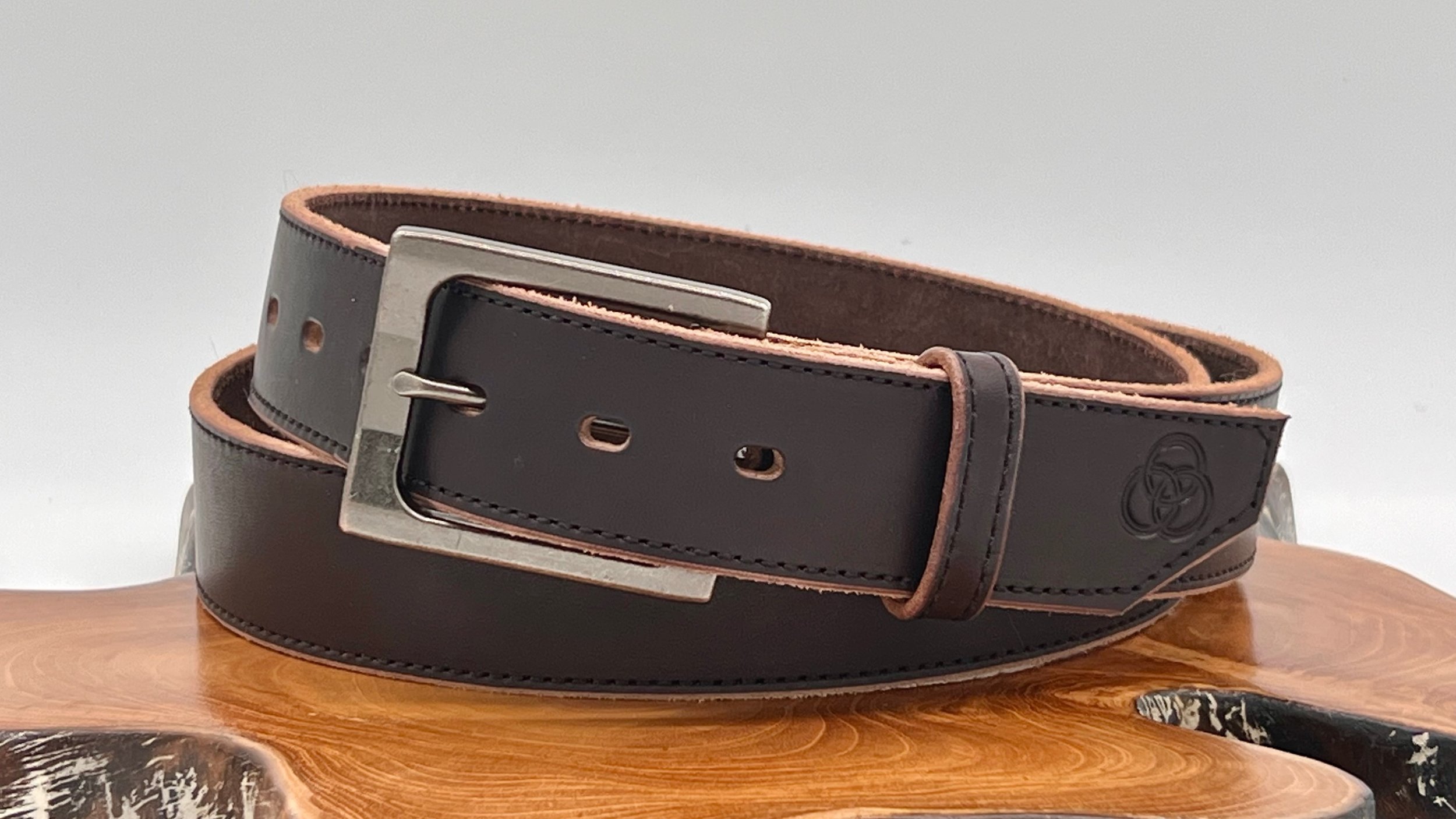 A black leather belt with a metal buckle, placed on a wooden surface.