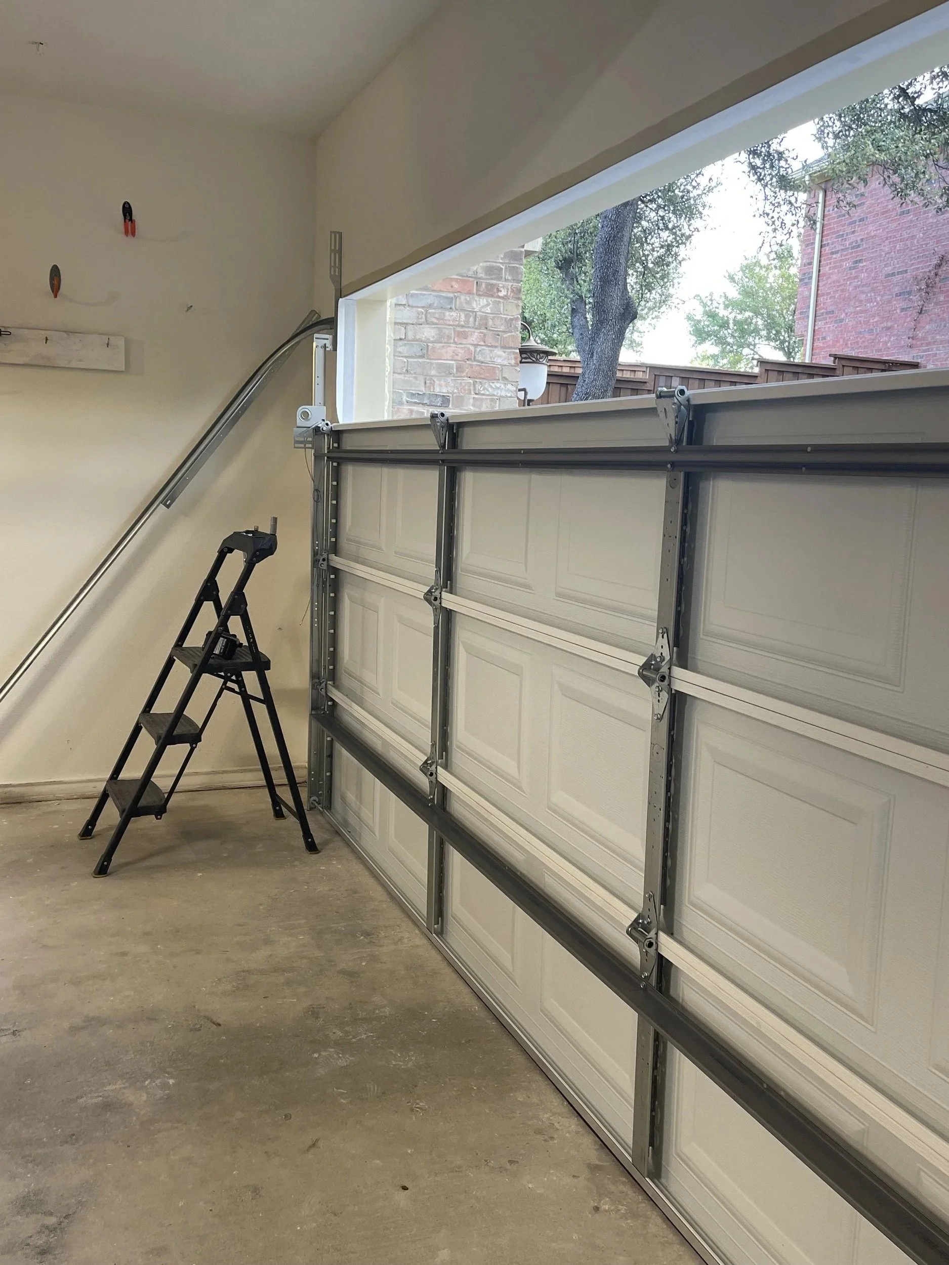 Inside a garage with a lifted garage door, a step ladder, and a wall with hooks and a rail.