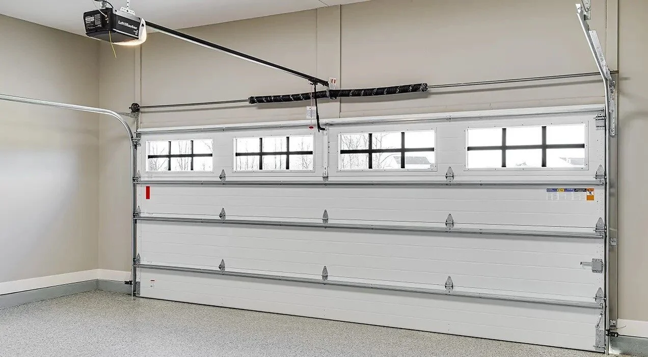Empty garage with a white overhead sectional garage door with windows, a ceiling-mounted garage door opener, and a textured light gray floor.