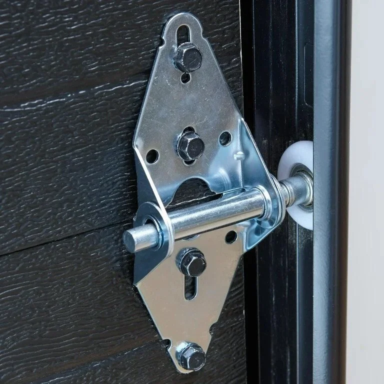 A metal door strike plate with latch bolt installed on a dark wooden door frame.