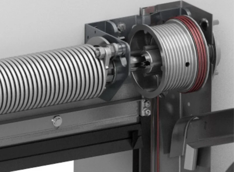 Close-up view of a mechanical device with a large, coiled metal spring and a red rubber ring, mounted on a gray metal frame.