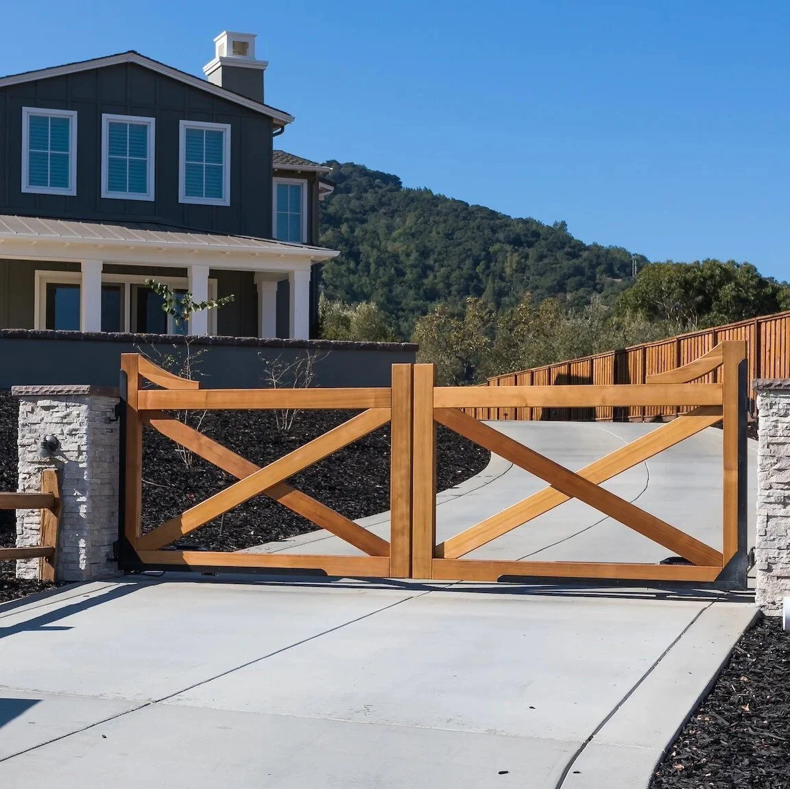 Wooden driveway gate in front of a modern house with a mountain background.