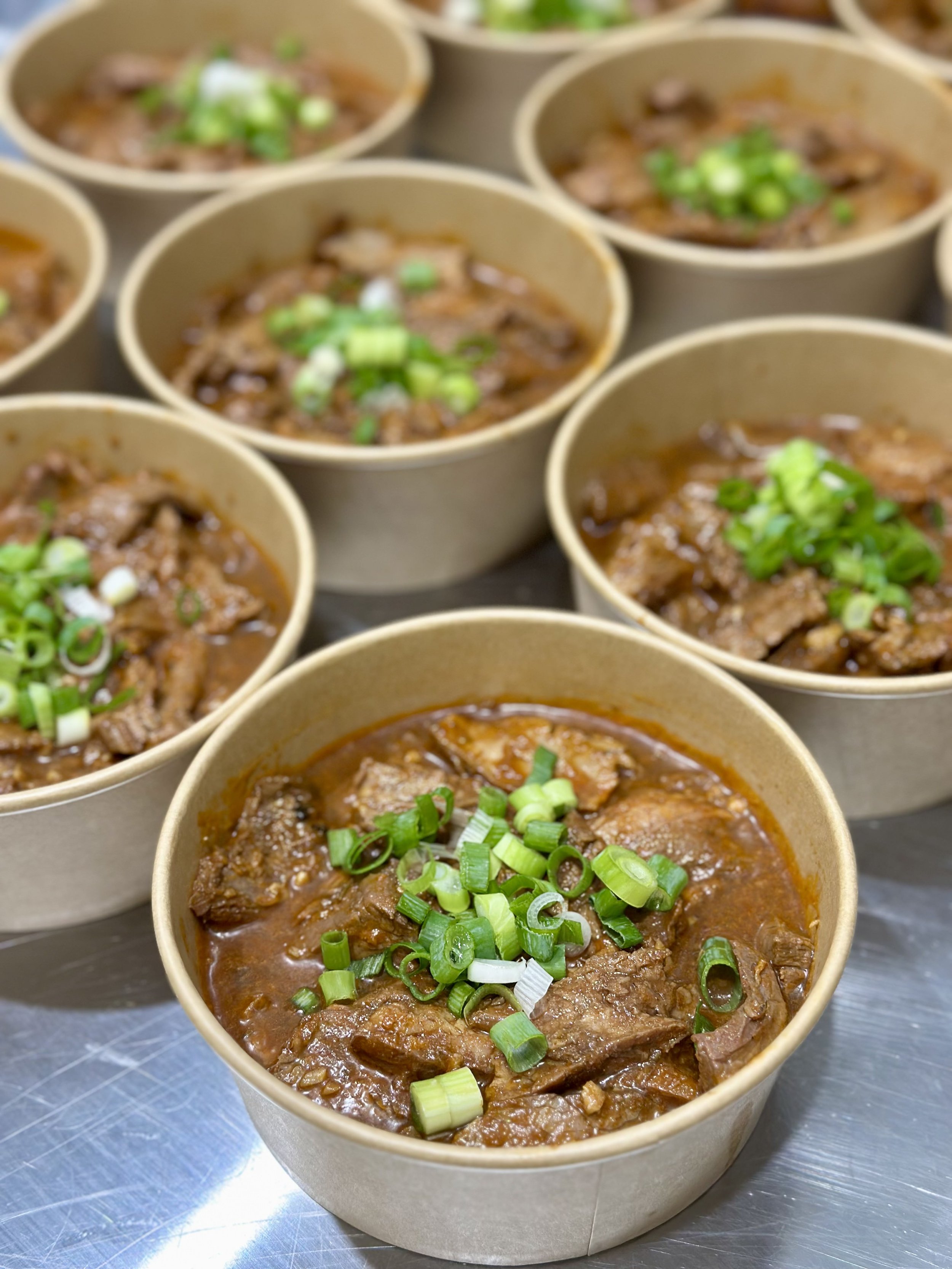 Carne Asada with Flank Steak and topped with fresh cut scallions being plated in the commercial kitchen, getting ready to be delivered to people's homes for a Dinner Mama's meal care package.