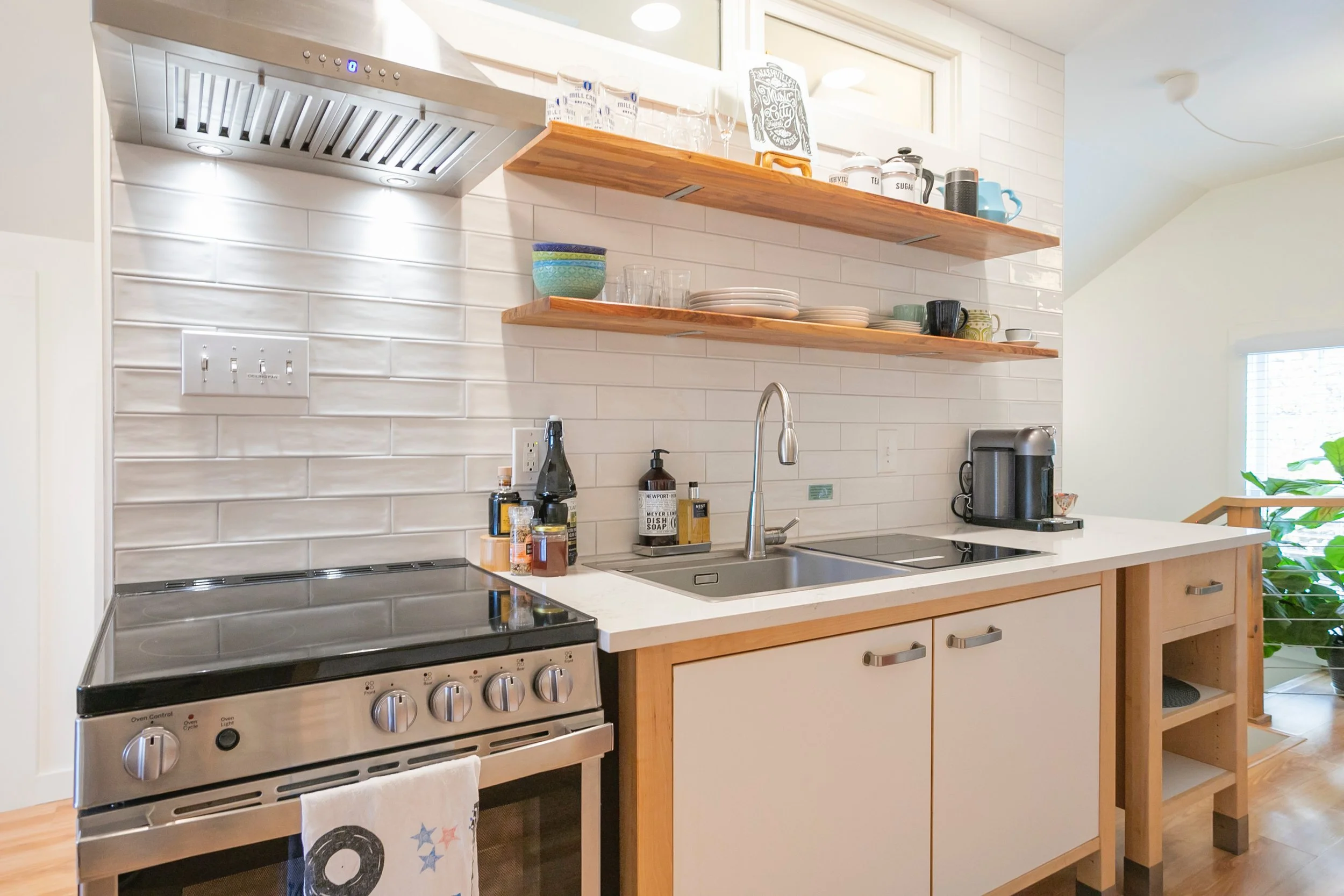 Modern kitchen with stainless steel stove, open shelves with dishes and bowls, a double sink, coffee machine, and various kitchen items on the counter.
