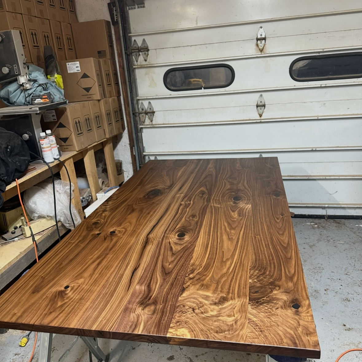 Wooden table in a garage with tools and boxes on shelves in the background.
