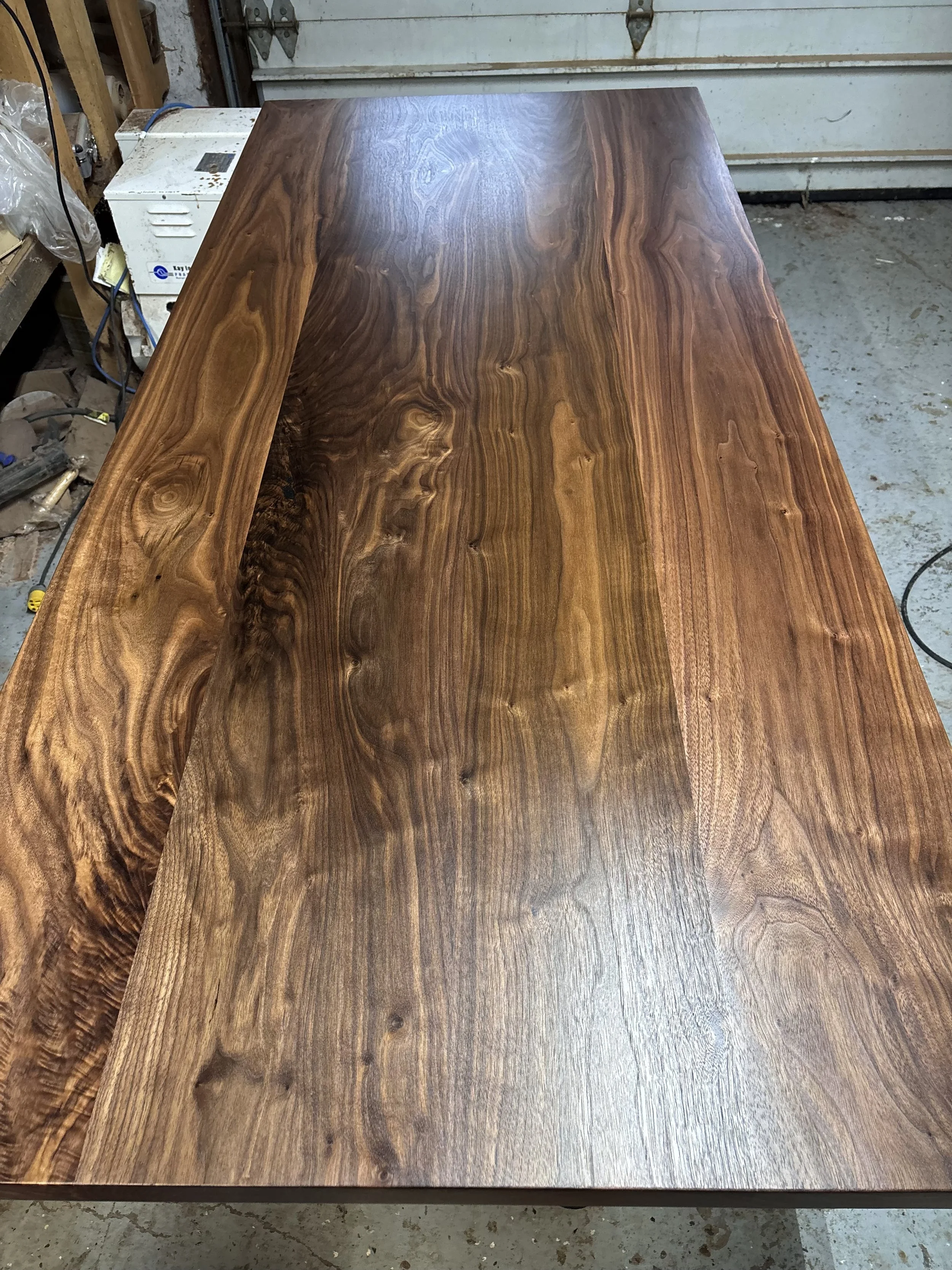 A polished solid wood tabletop with visible natural wood grain, placed on a work surface in a workshop.