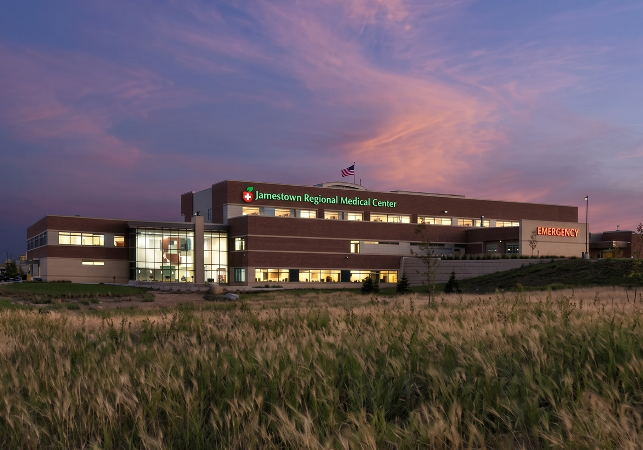 Exterior view of Jamestown Regional Medical Center at dusk, with the building illuminated and the sky showing pink and purple hues.