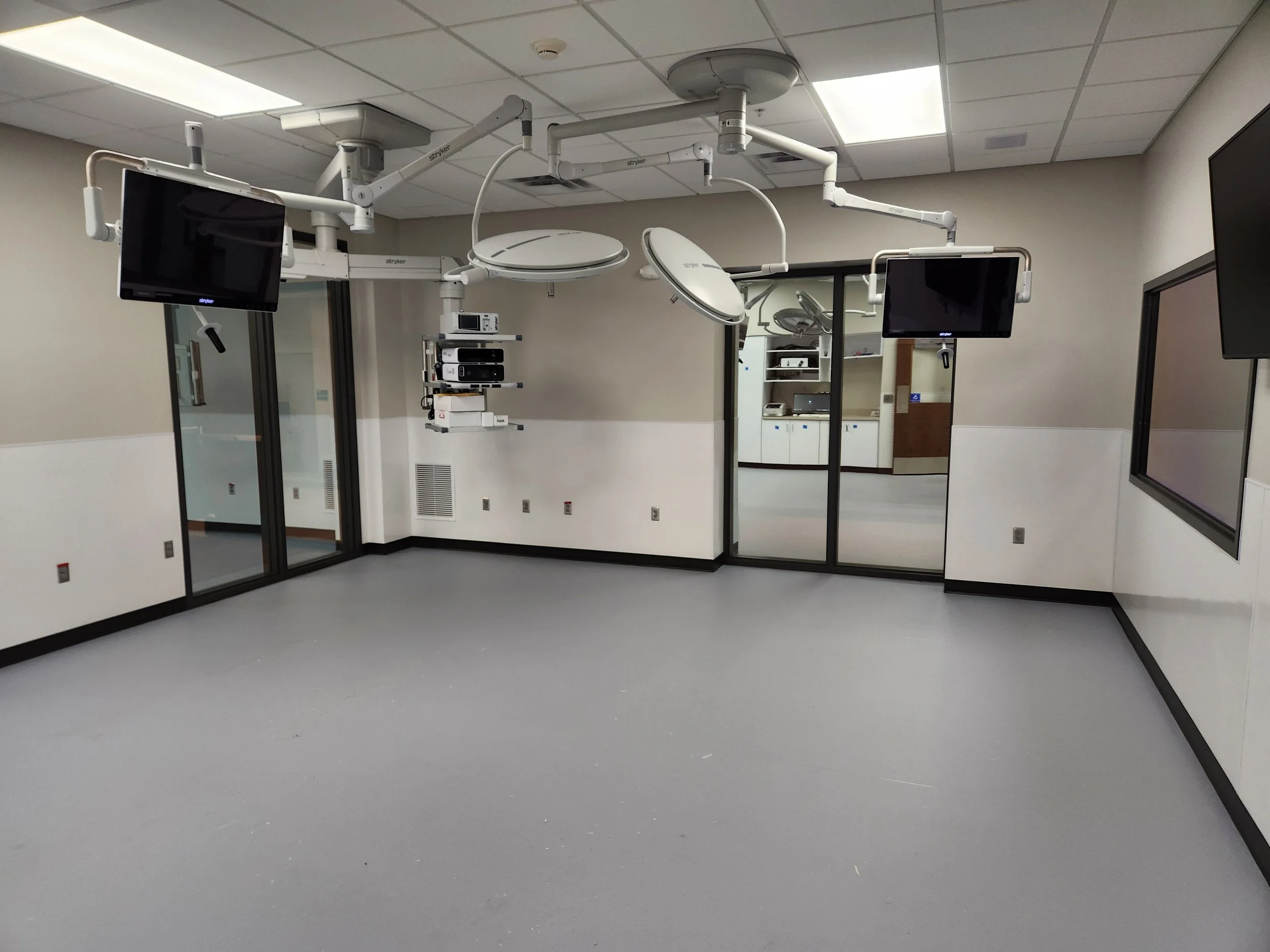 Empty hospital operating room with ceiling-mounted surgical lights, monitors, and medical equipment.